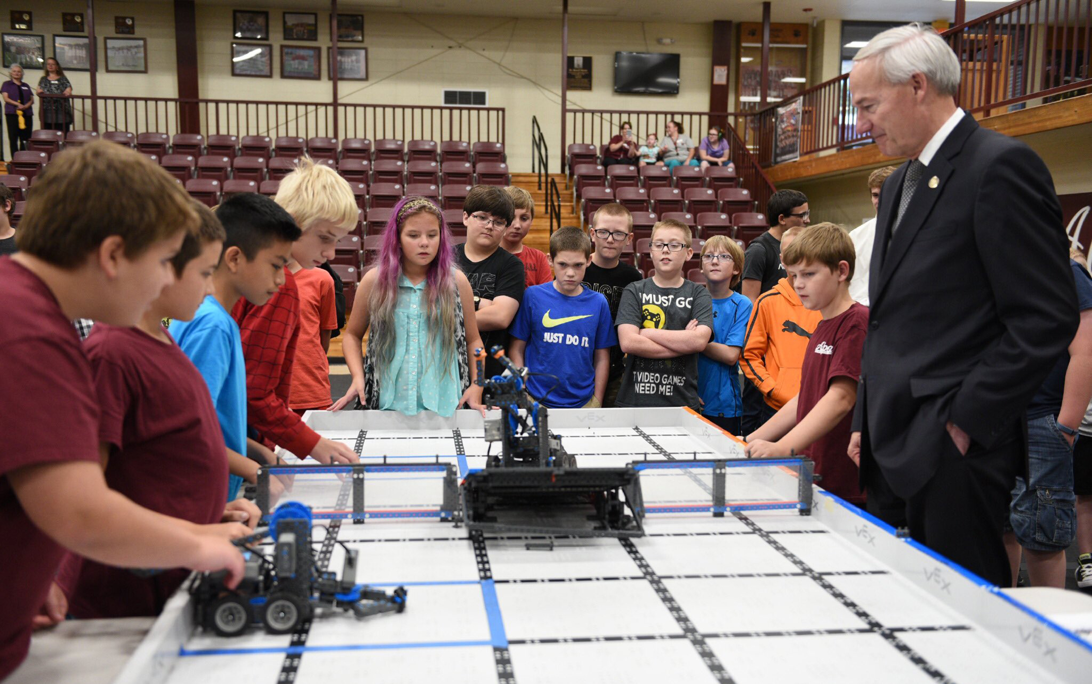 Asa Hutchinson, on the right, stands with a dozen students around a robotics table