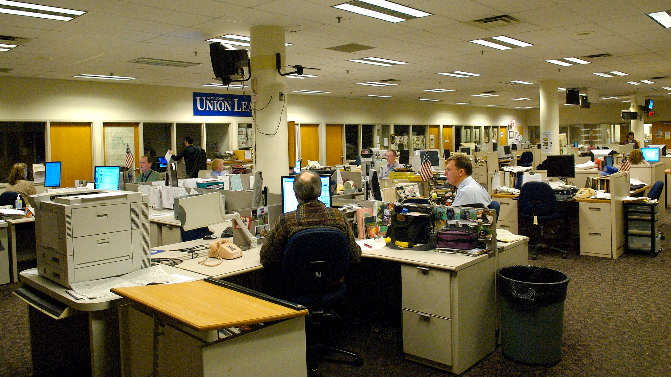 Journalists sitting in cubicles work in front of their computers