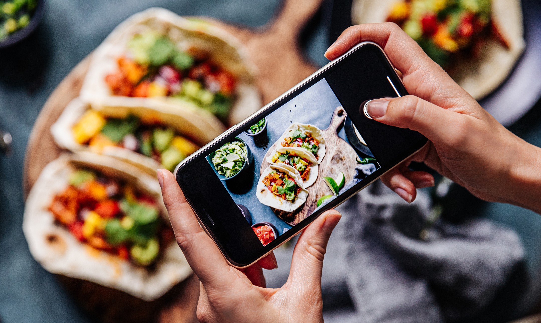 Hand of a chef taking photograph of tacos on table with a mobile phone. Hands of cook photographing Mexican food