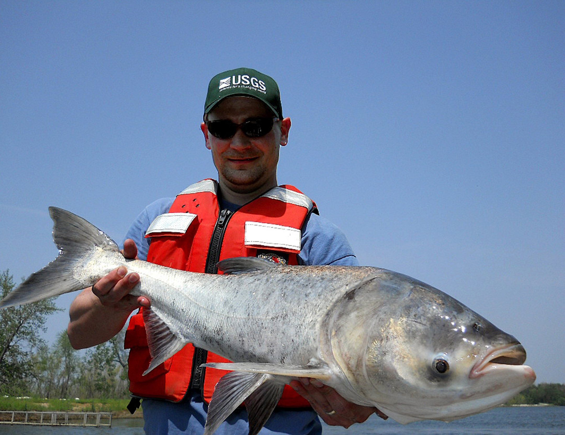 Man in sunglasses and a life vest smiles while holding a large fish