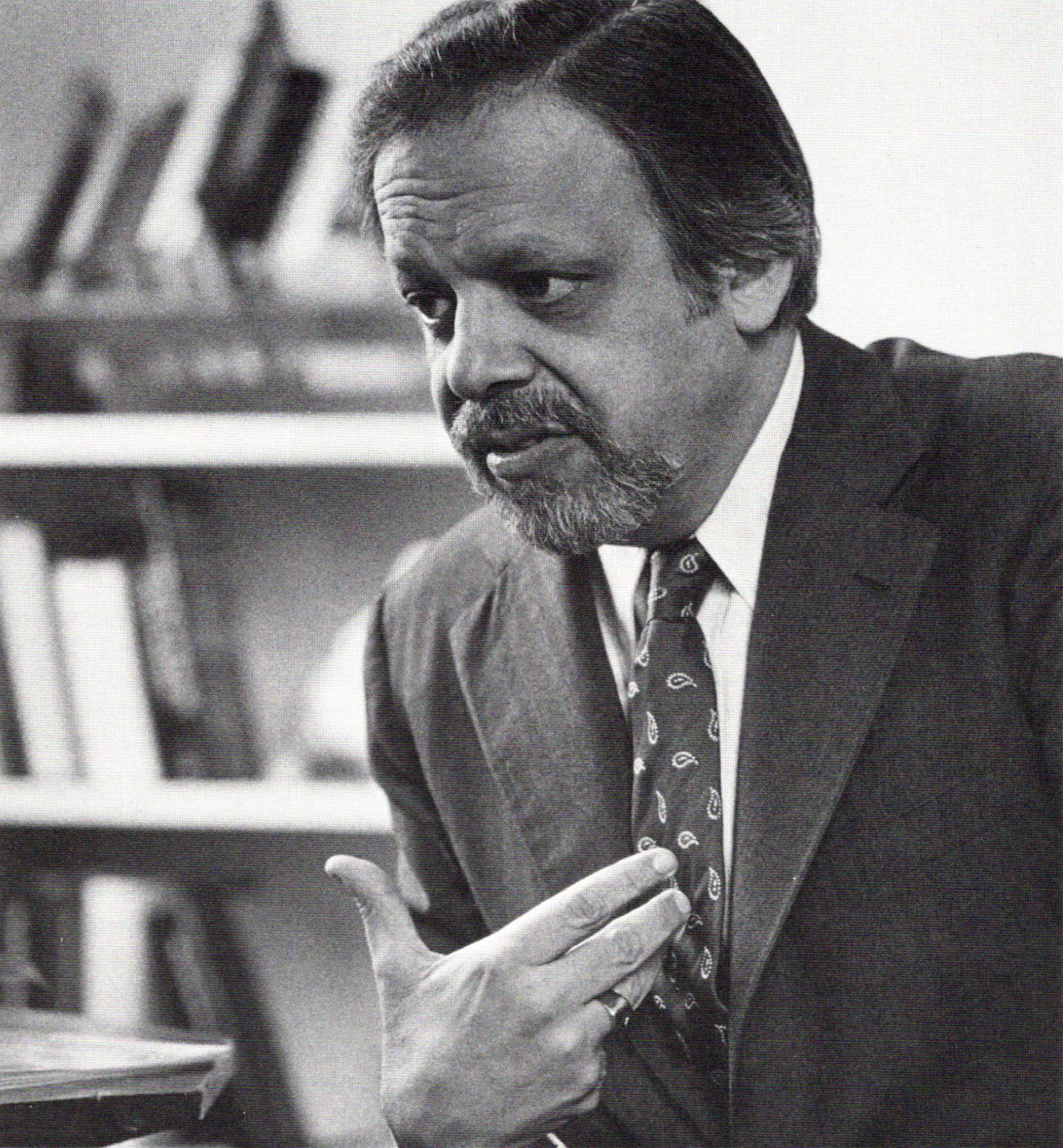 Black and white photo of A. Bartlett Giamatti pointing at himself while speaking in his office