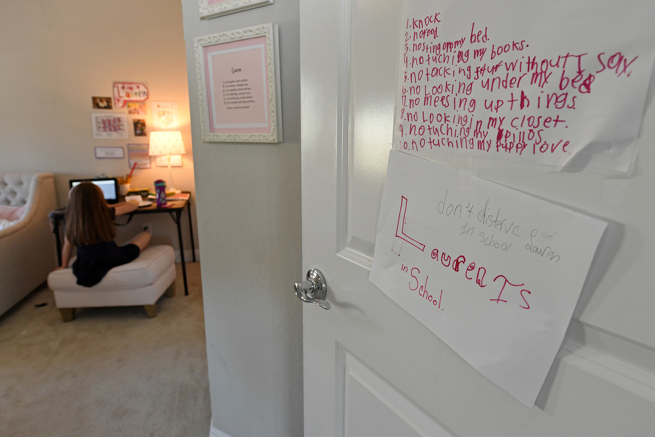 Photo of a bedroom door, open, with a young girl in the background working on a computer at a desk