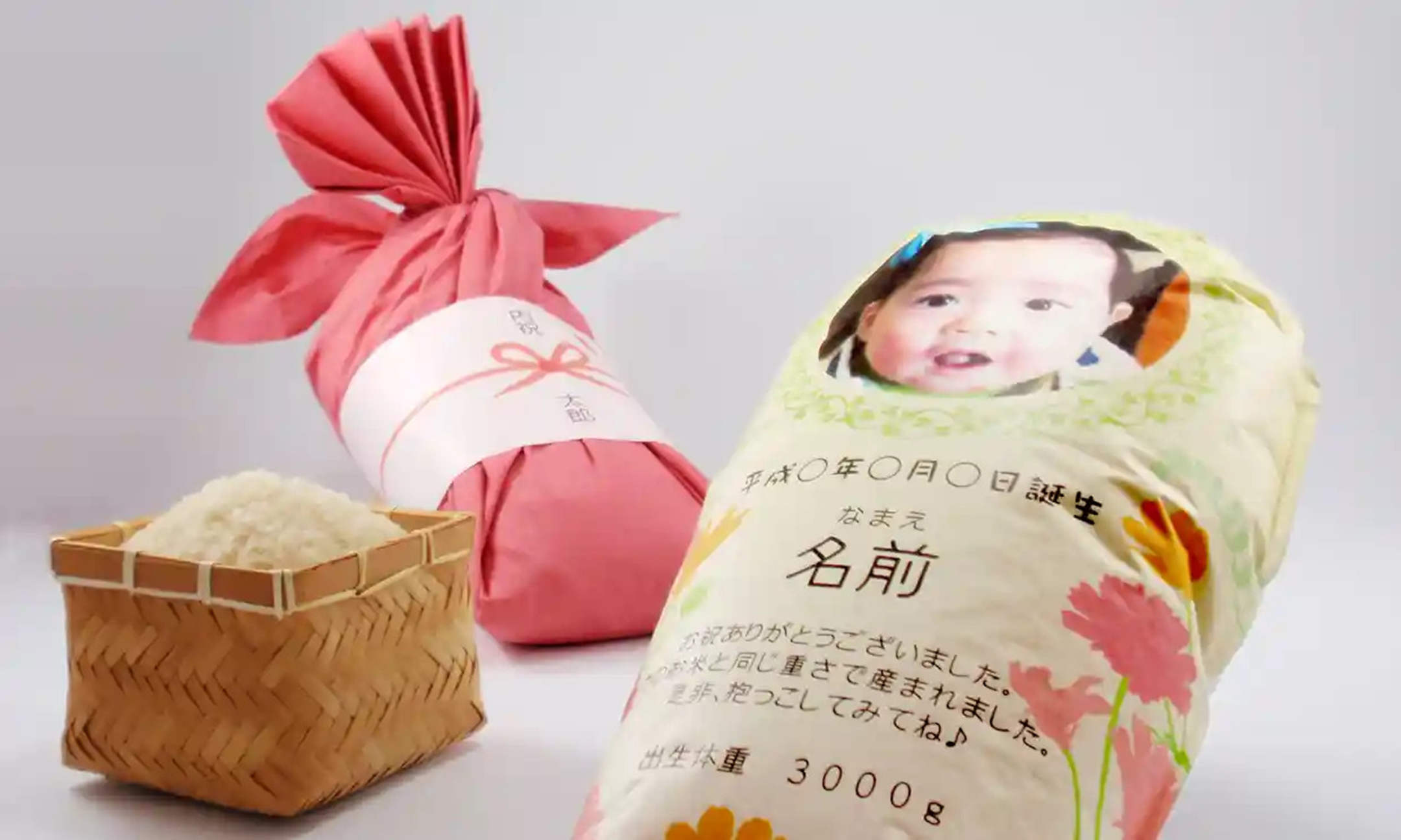 Bag of rice in the form of a newborn in a blanket, on the right; a red wrapped blanked in the middle background, and a box of cooked rice on the left
