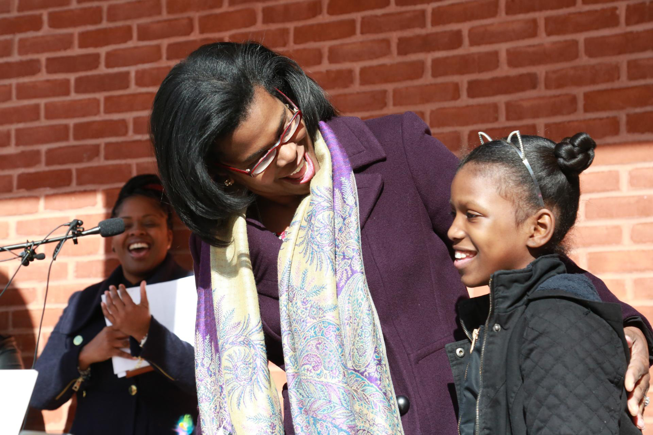 Sonja Santelises, in a winter coat and scarf, smiles as she puts her arm around a smiling student