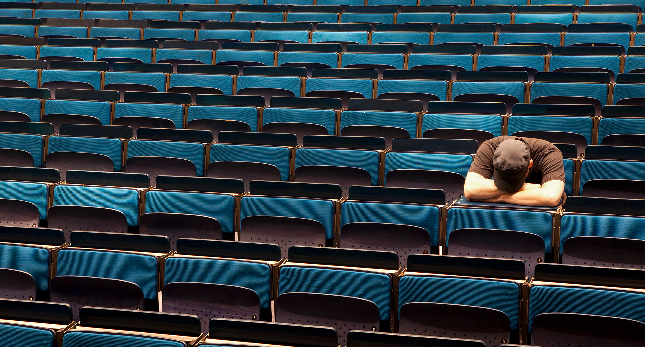 A man sitting in an empty university auditorium with his head resting in his arms 
