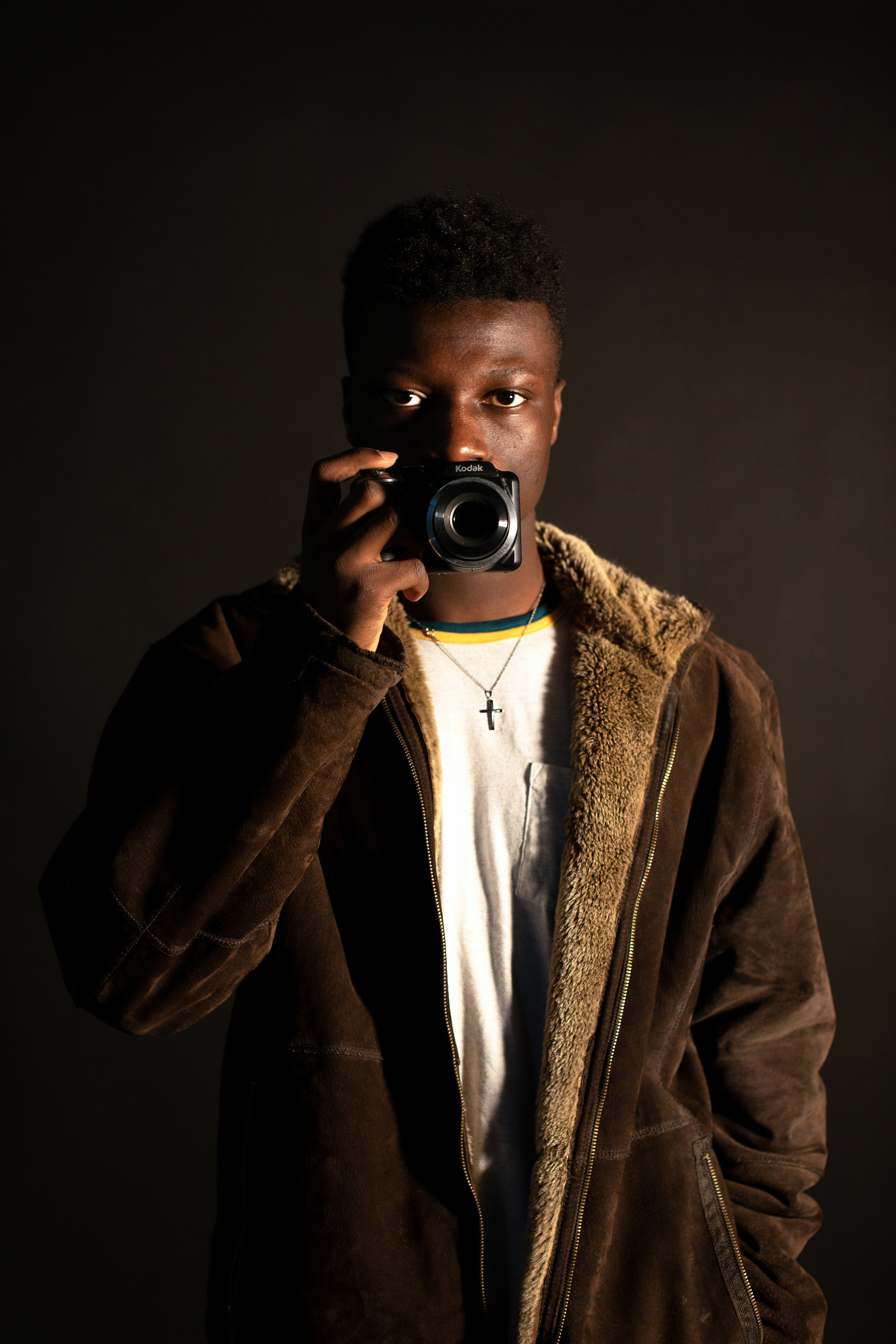 Full body Self-portrait photograph of a young black man in a coat against a black background