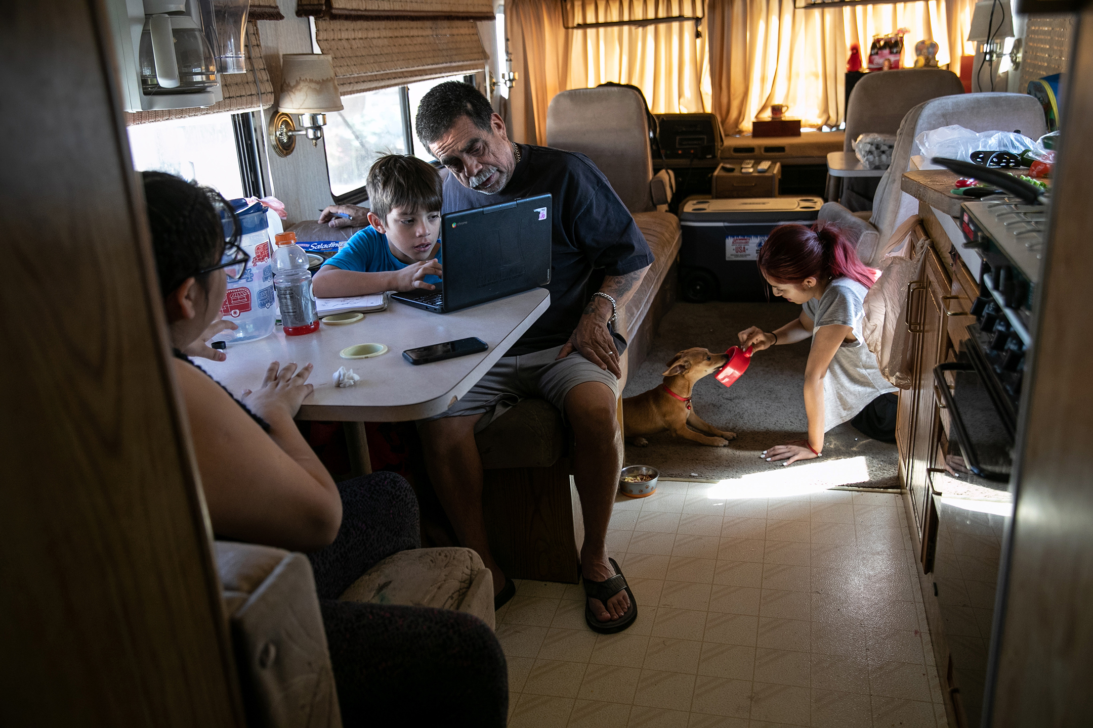 Older man helps a young boy working on a laptop in a cluttered RV