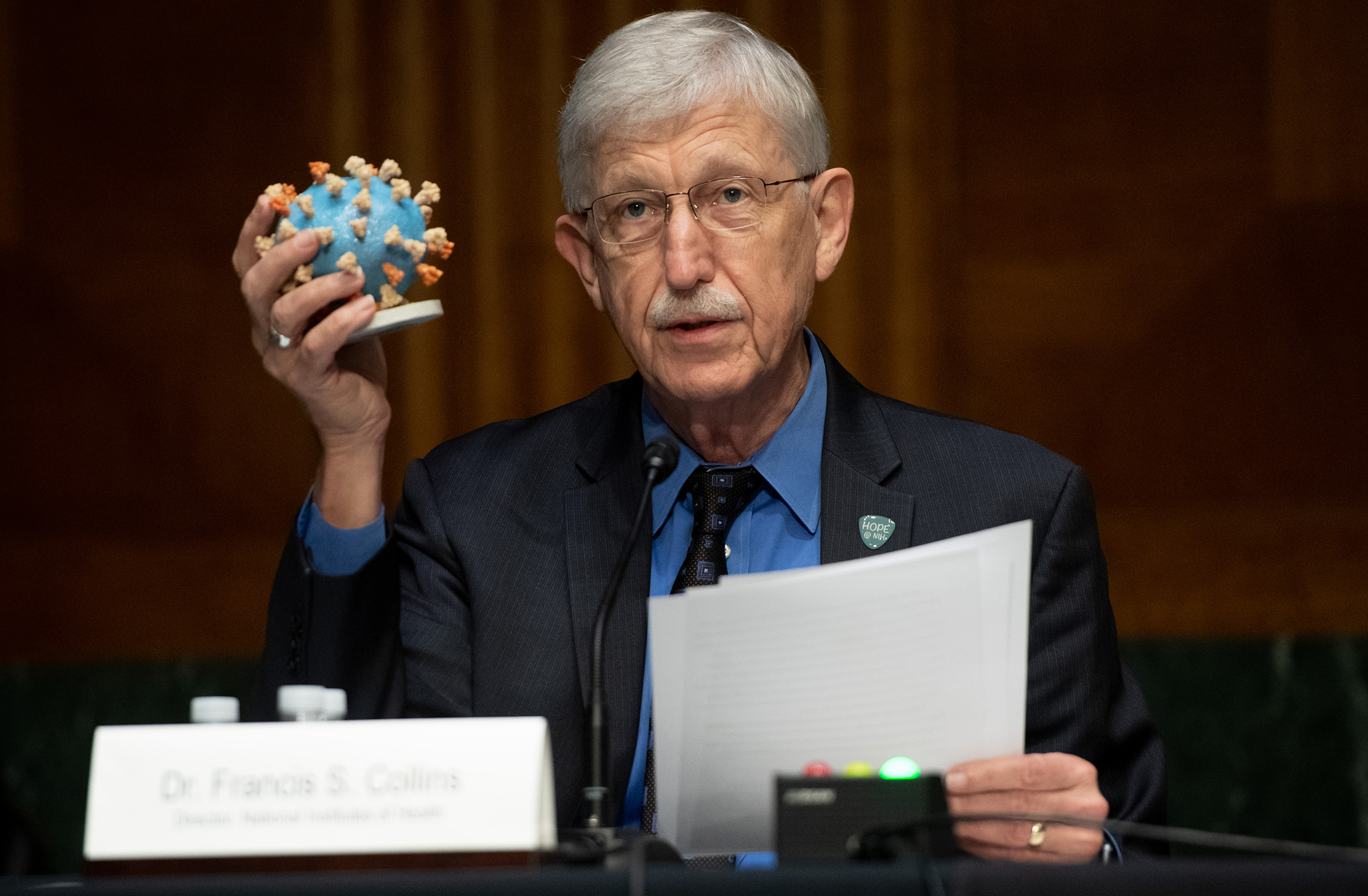 Older white man sitting at a table holding a model of a germ
