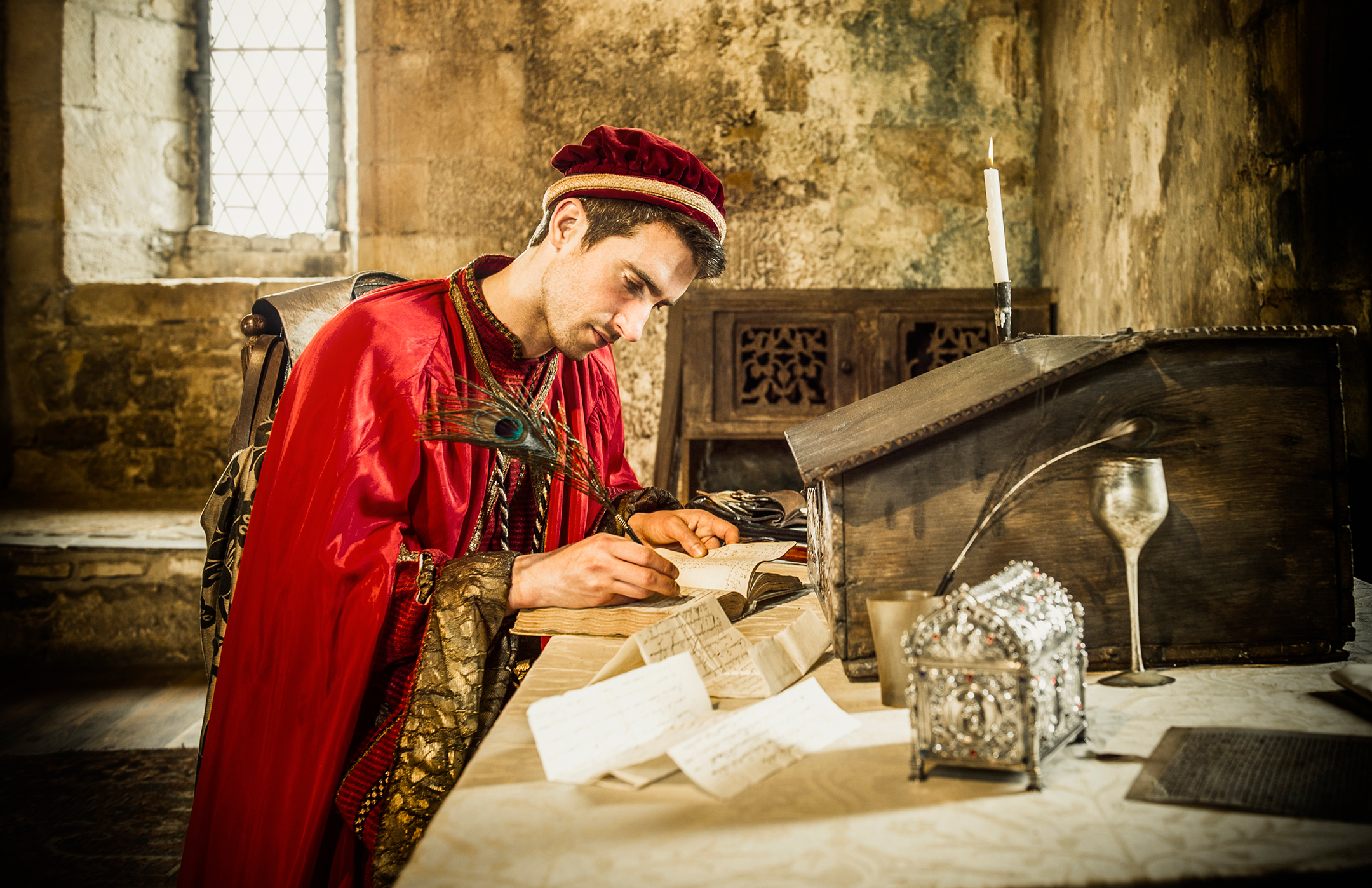 Caucasian man in medieval costume reading in castle and writing with a quill pen