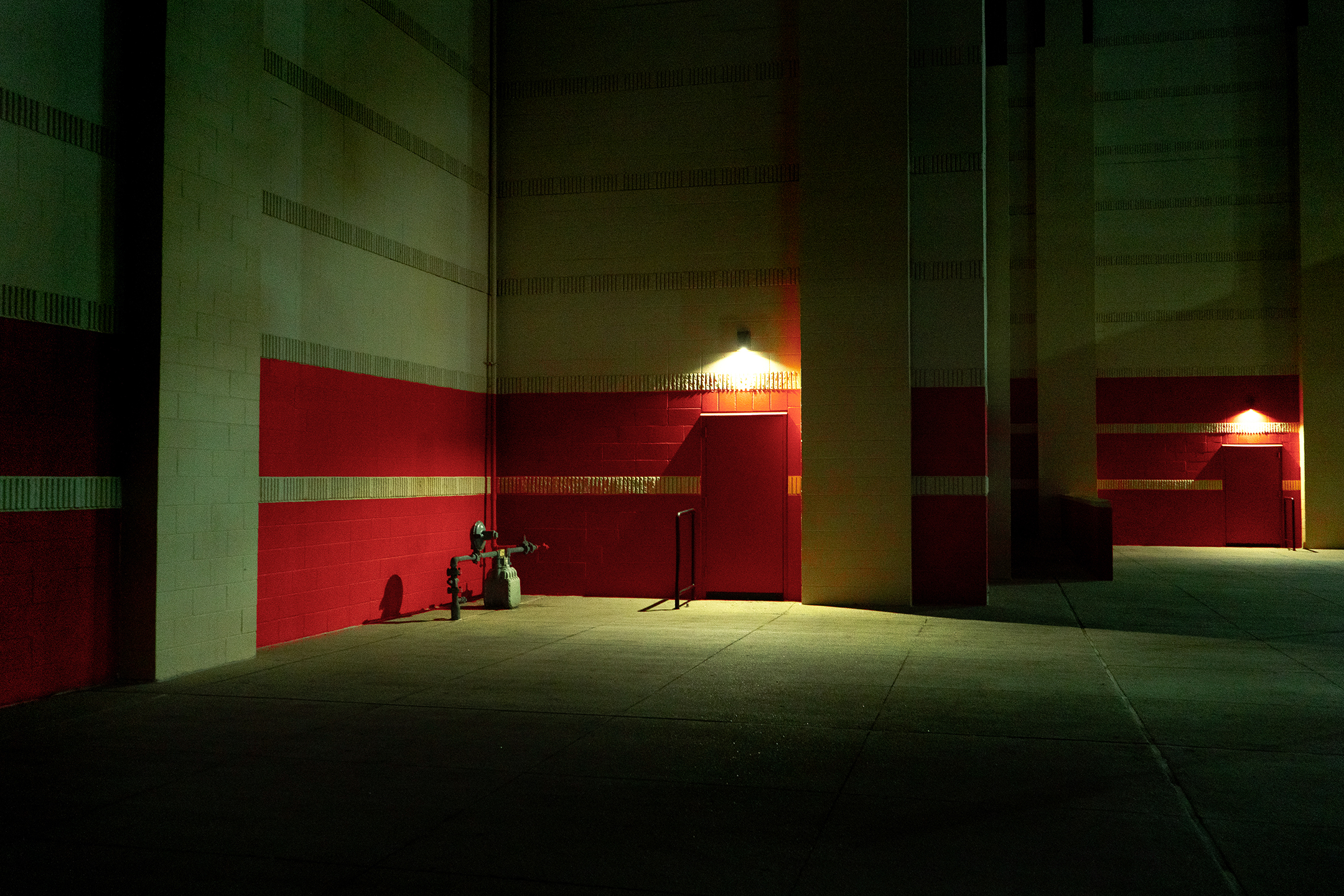 Photo of a building at night highlight a band of red paint and a gas meter under fluorescent light