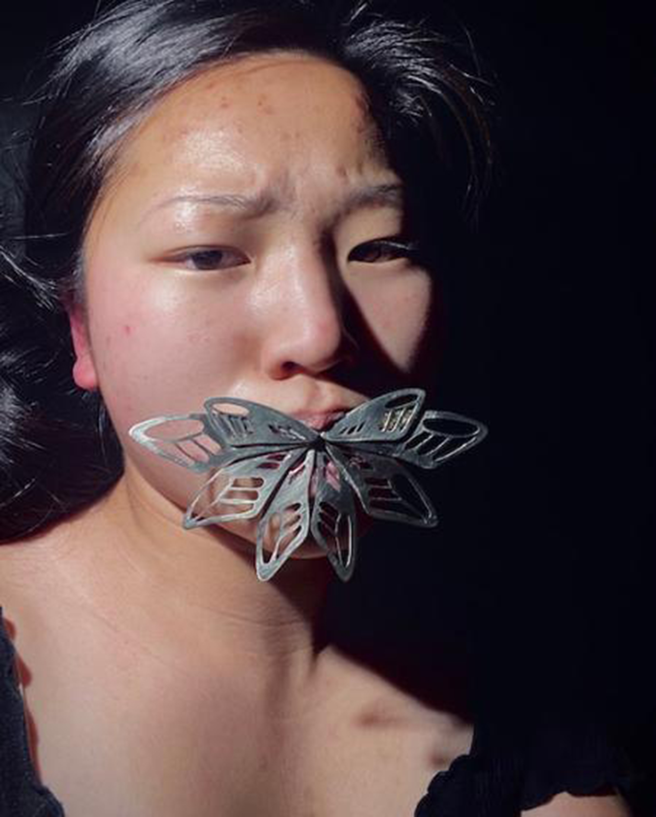 Photo of a young Asian woman with a metal flower in her mouth