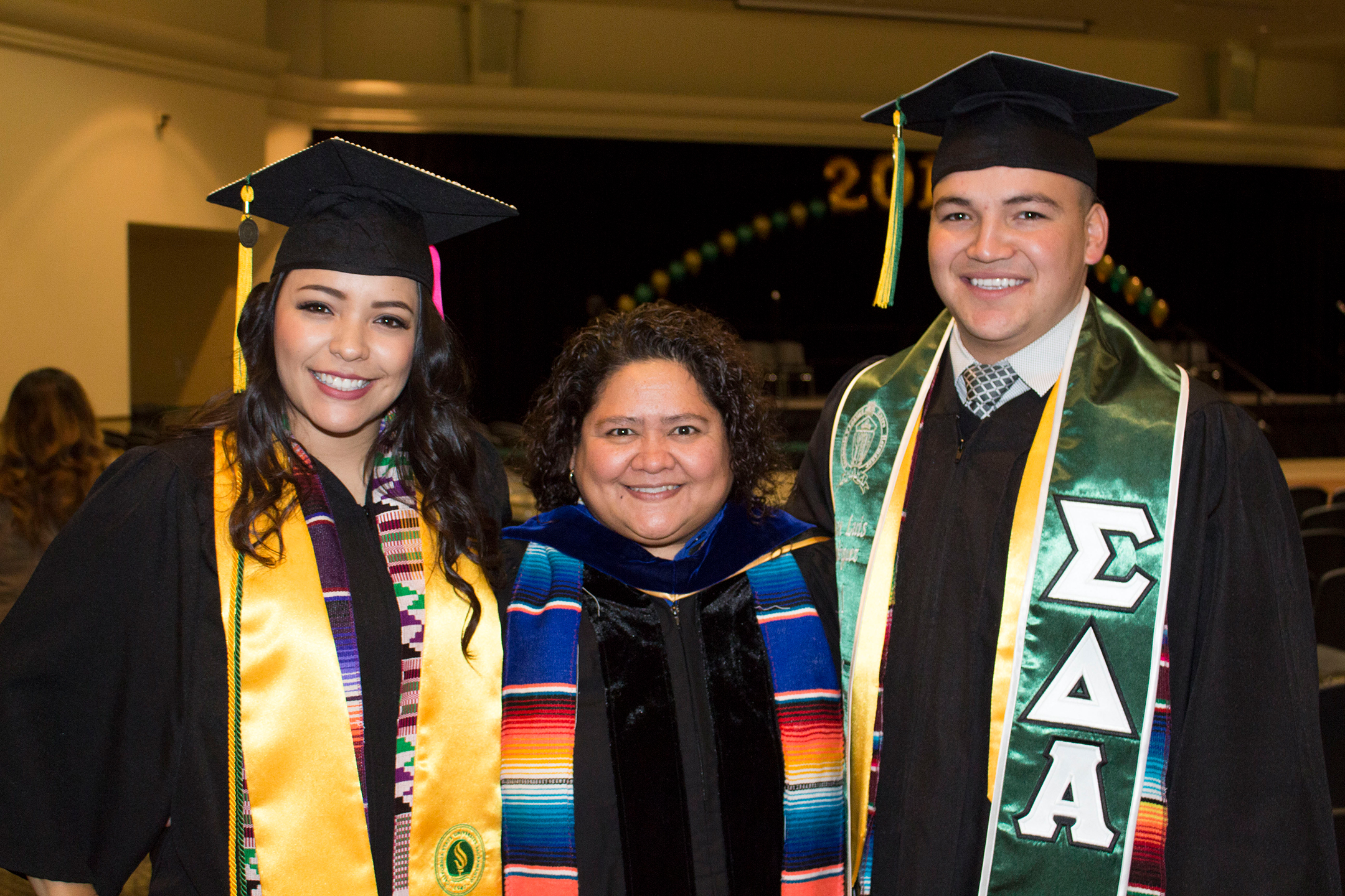 Deborah Santiago stands between two college graduates, a female on the left and a male on the right, after a graduation ceremony