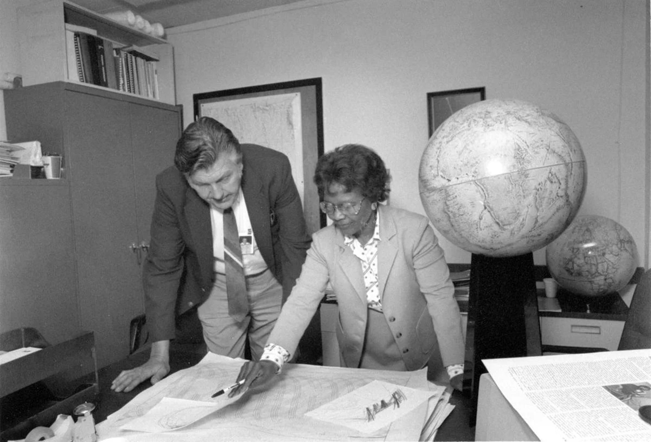 Black and white photo of a white man and black woman looking at a map on a desk