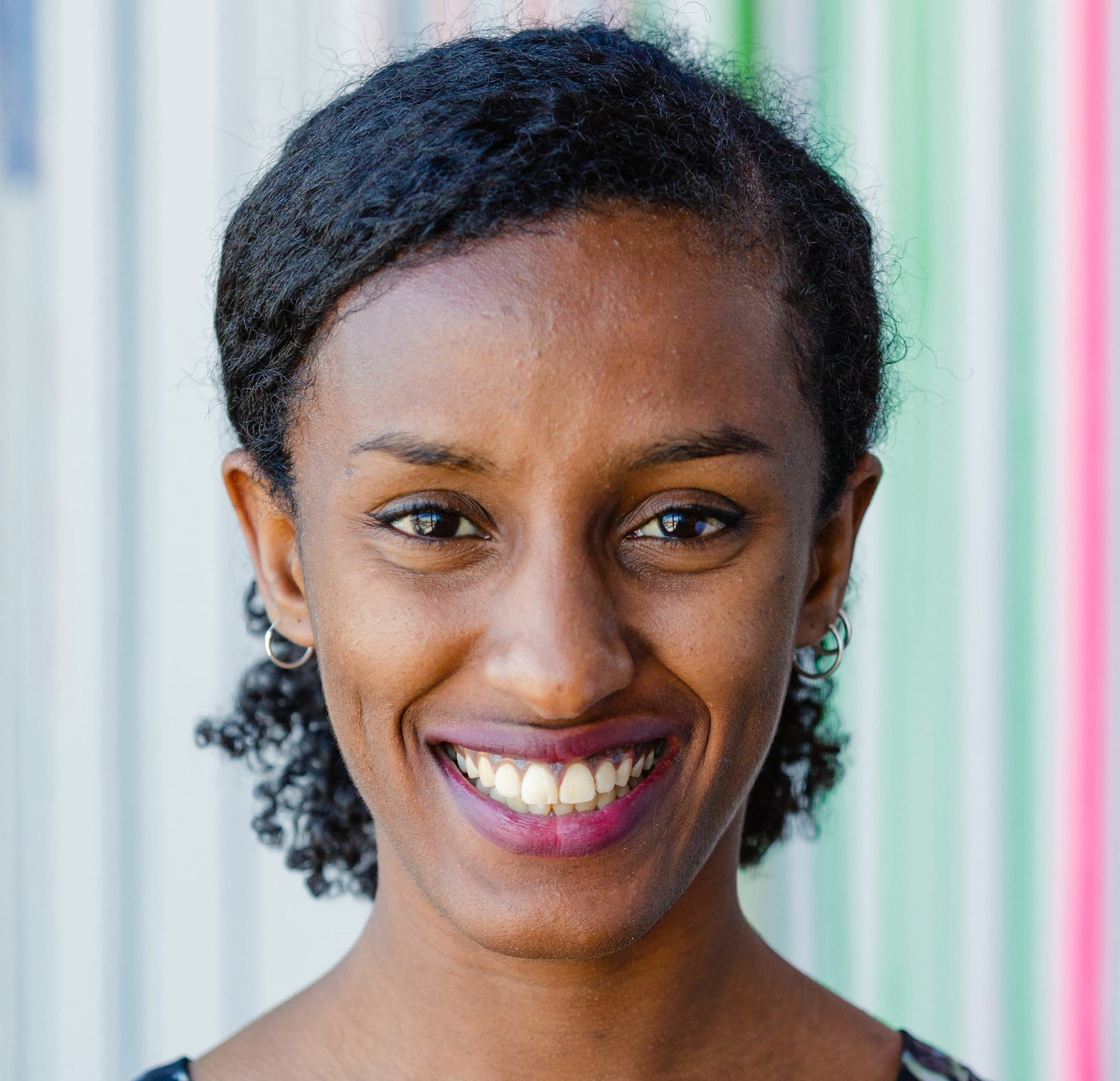 Photo of Rediet Abebe smiling against a striped background 