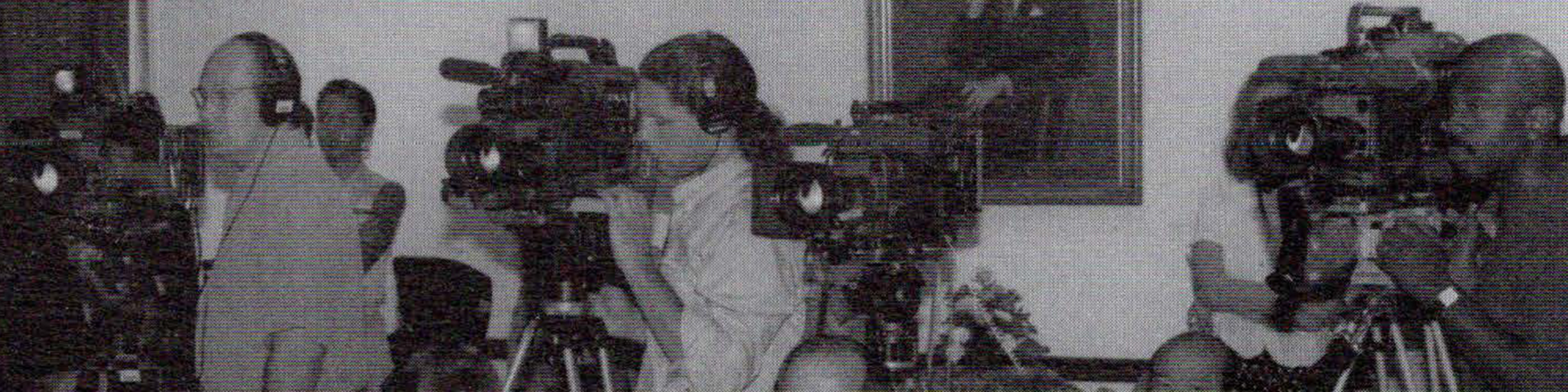 Black and white photo of cameraman at the back of a room standing with video cameras