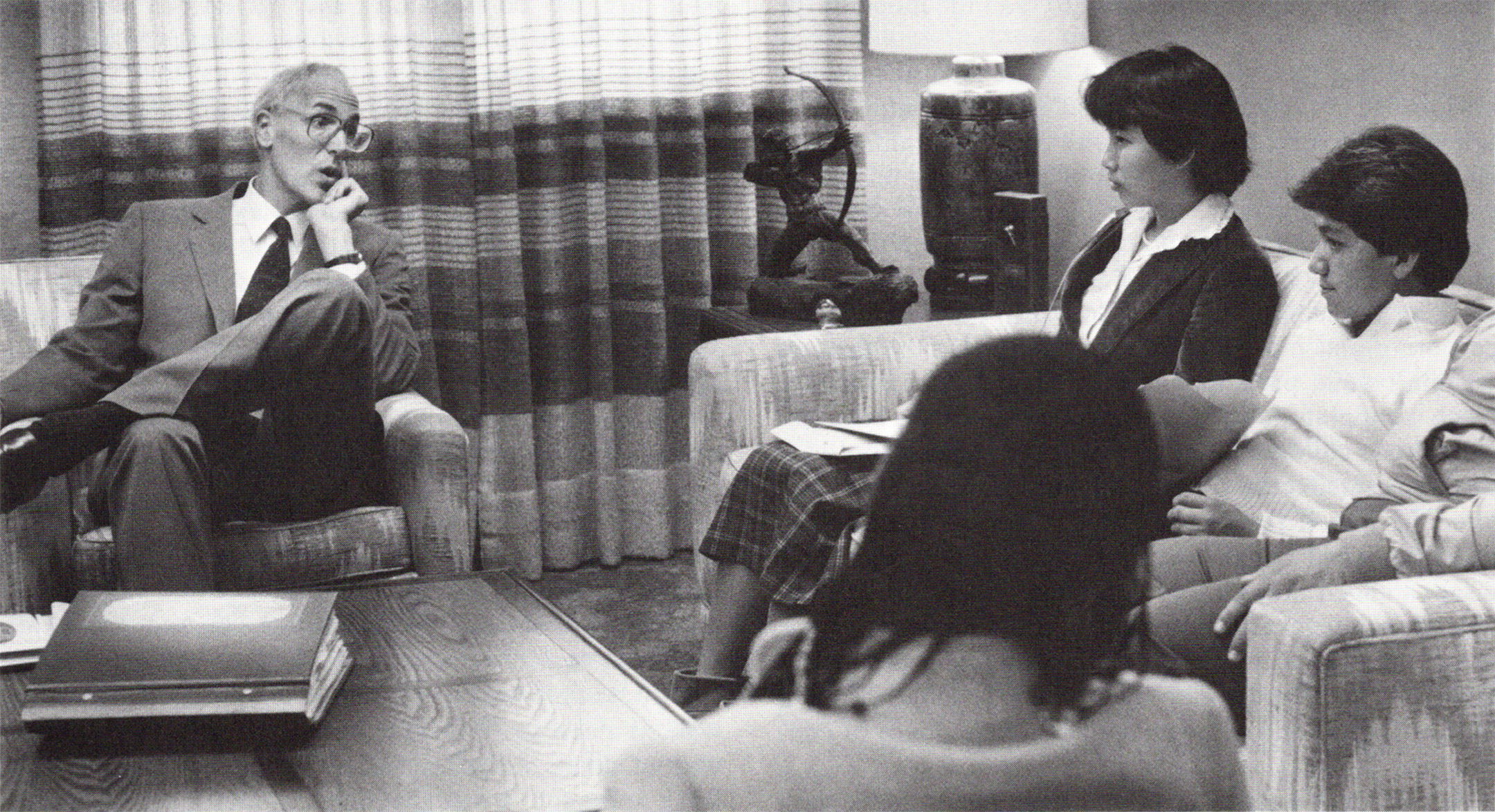 Black and white photo of Bill Honig, on left, speaking with three students in an office