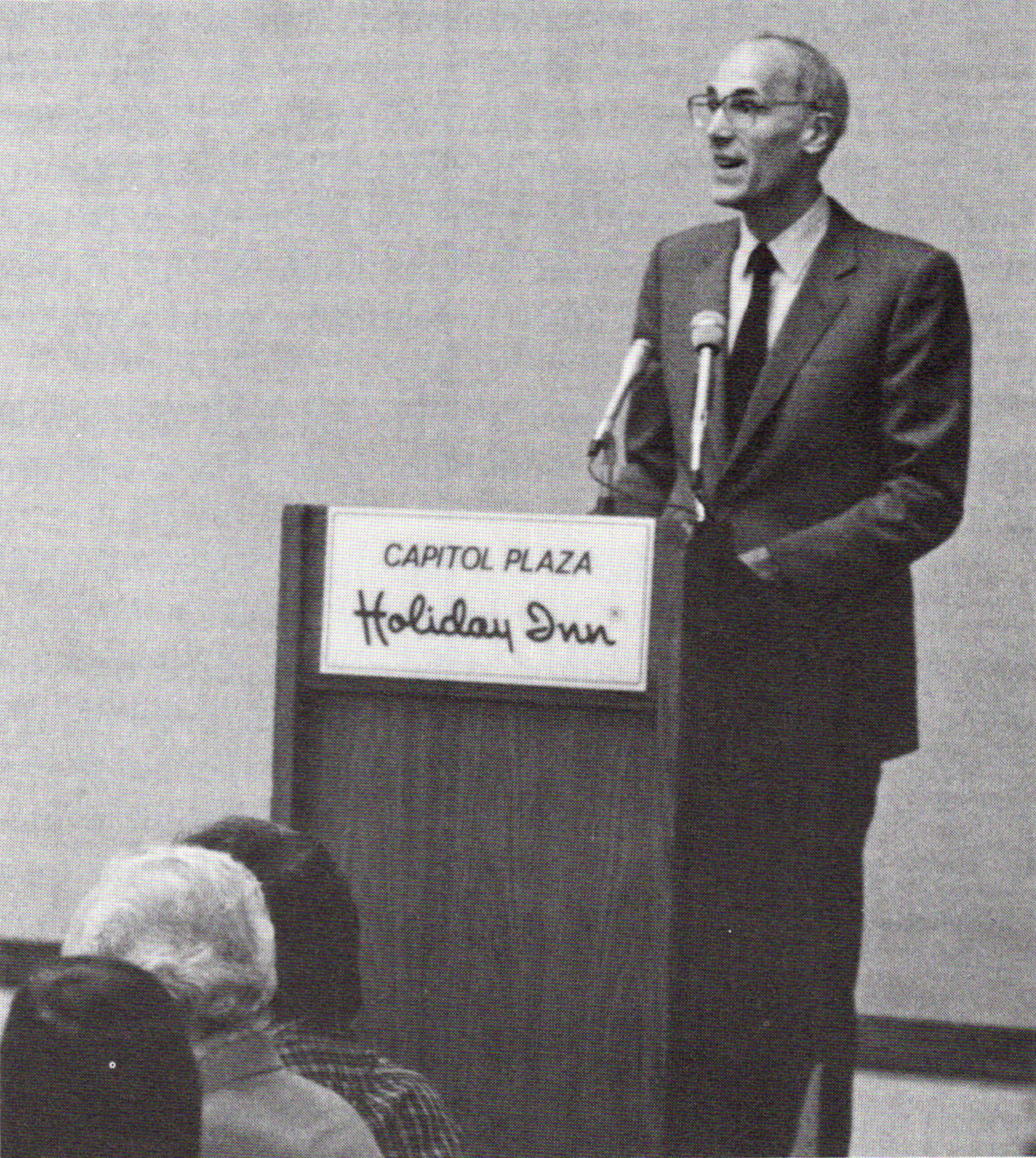Black and white photo of Bill Honig speaking from a lectern