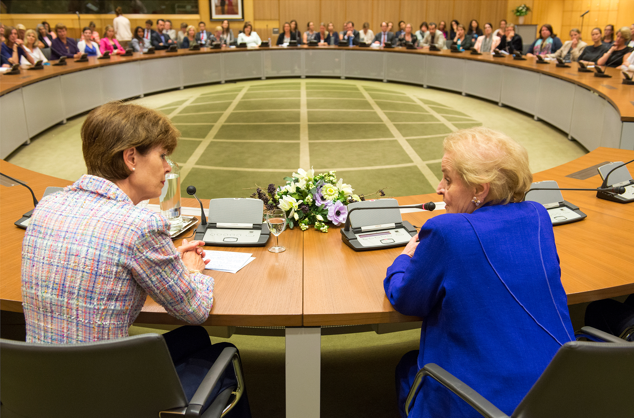 Madeleine Albright, at right, speaking to a woman as they sit at the head of a large ovular table