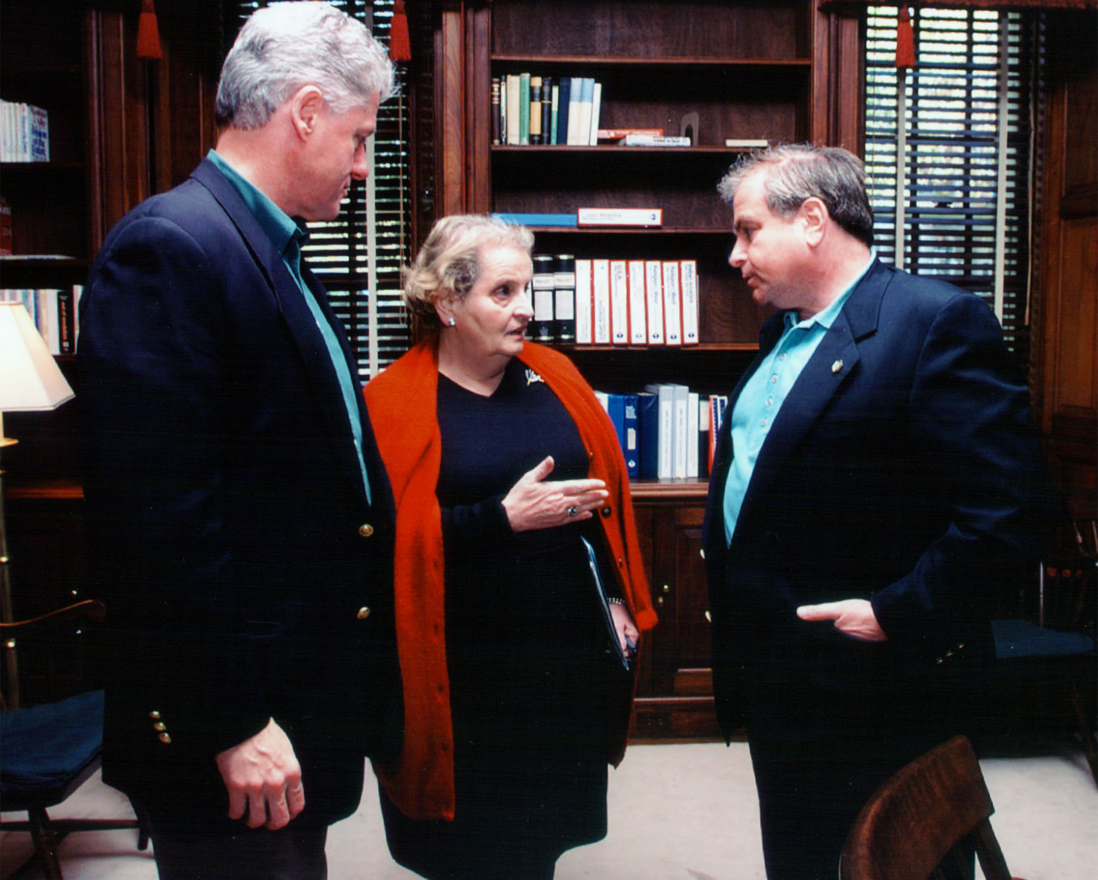 Madeleine Albright, center, speaking to two men in a wood-paneled library