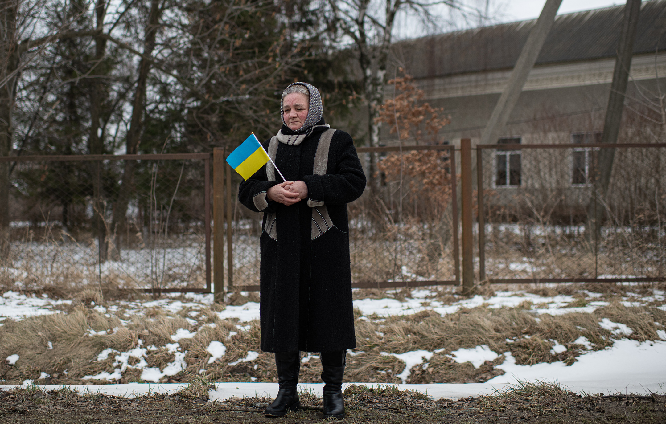 Woman in winter clothes holds a blue and yellow Ukrainian flag while standing alone on a road