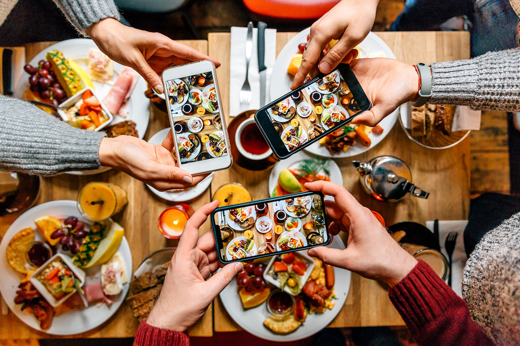 Friends taking pictures of food on the table with smartphones during brunch in restaurant 
