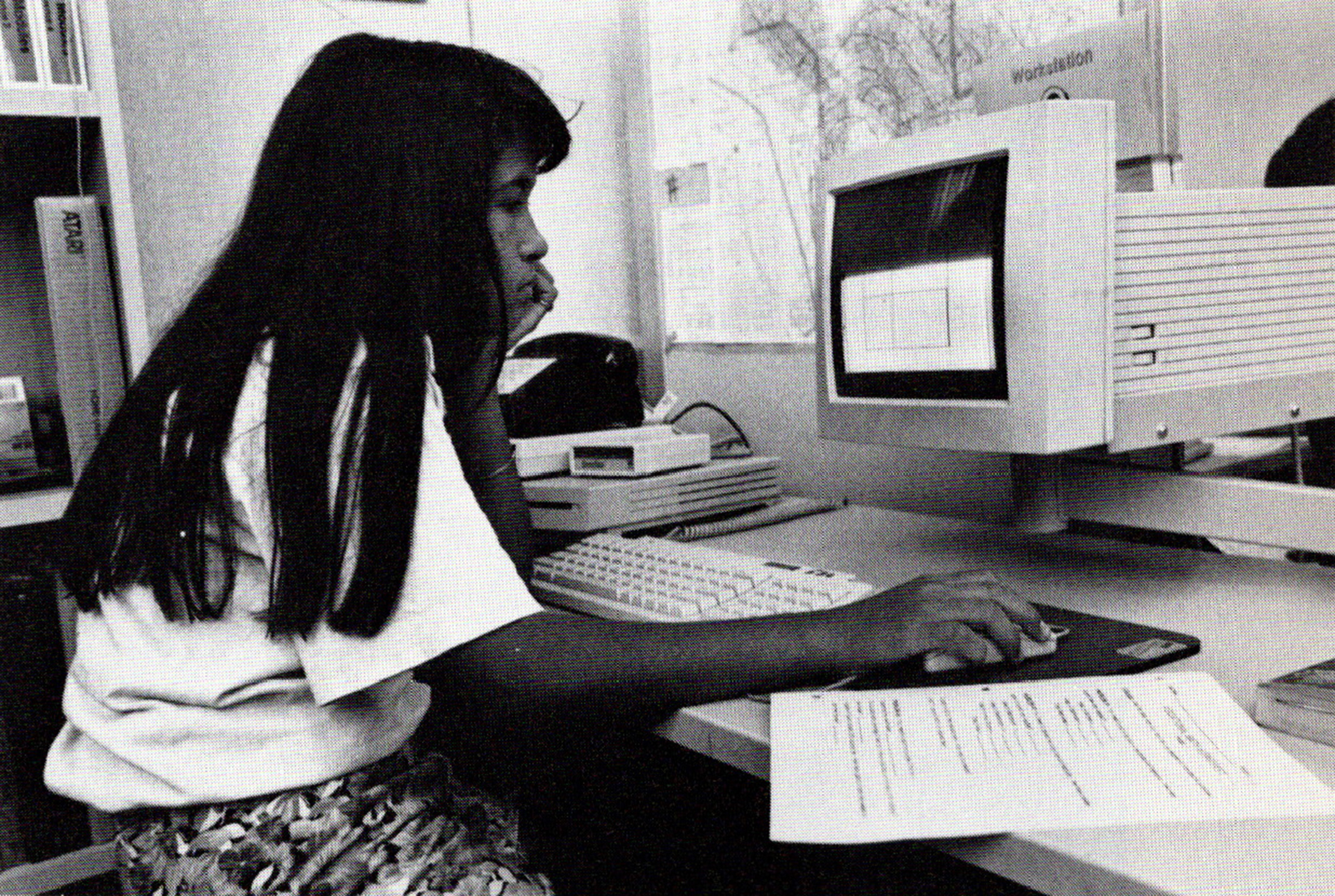 Black and white photo of a young female student sitting in front of an old desktop computer in her bedroom