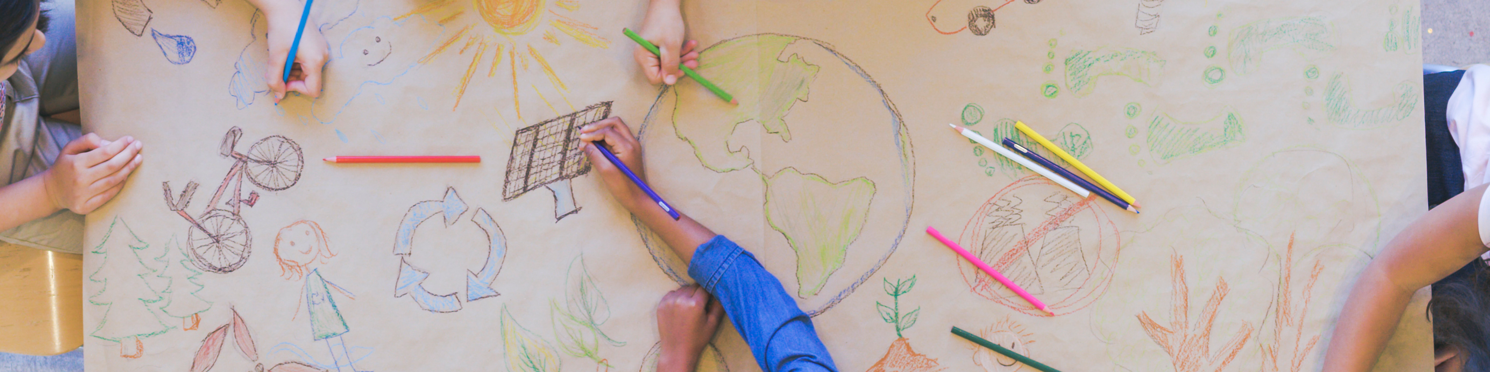 Aerial overhead view of a multi-ethnic group of elementary age children drawing using colored pencils to make a mural. The have colored a world map, objects found in nature, and symbols of environmental conservation.