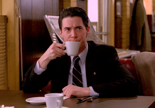 Animated gif of a man in a black suit drinking coffee and smiling