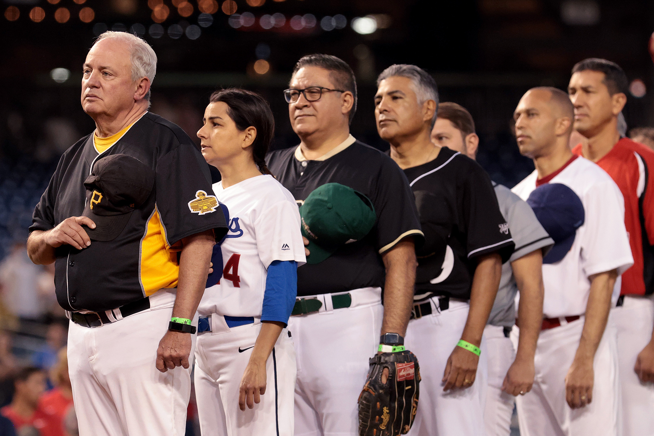 Row of seven congresspeople in baseball uniforms saluting the National Anthem