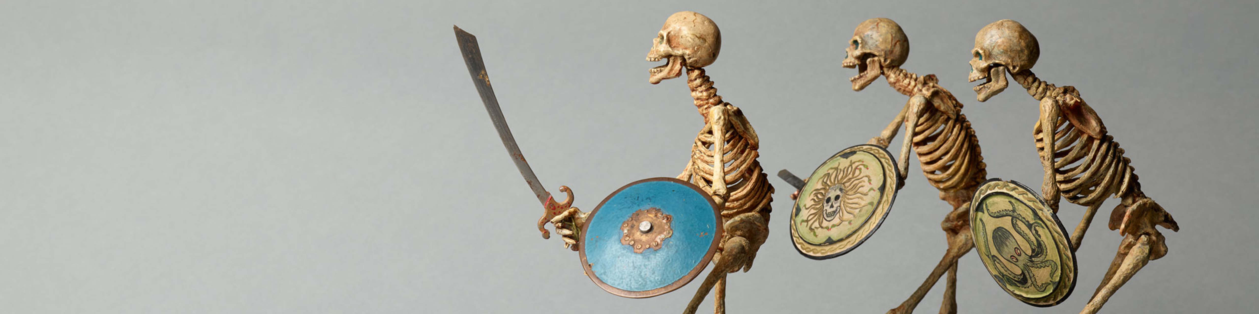 Three model skeletons in a row, holding swords and shields