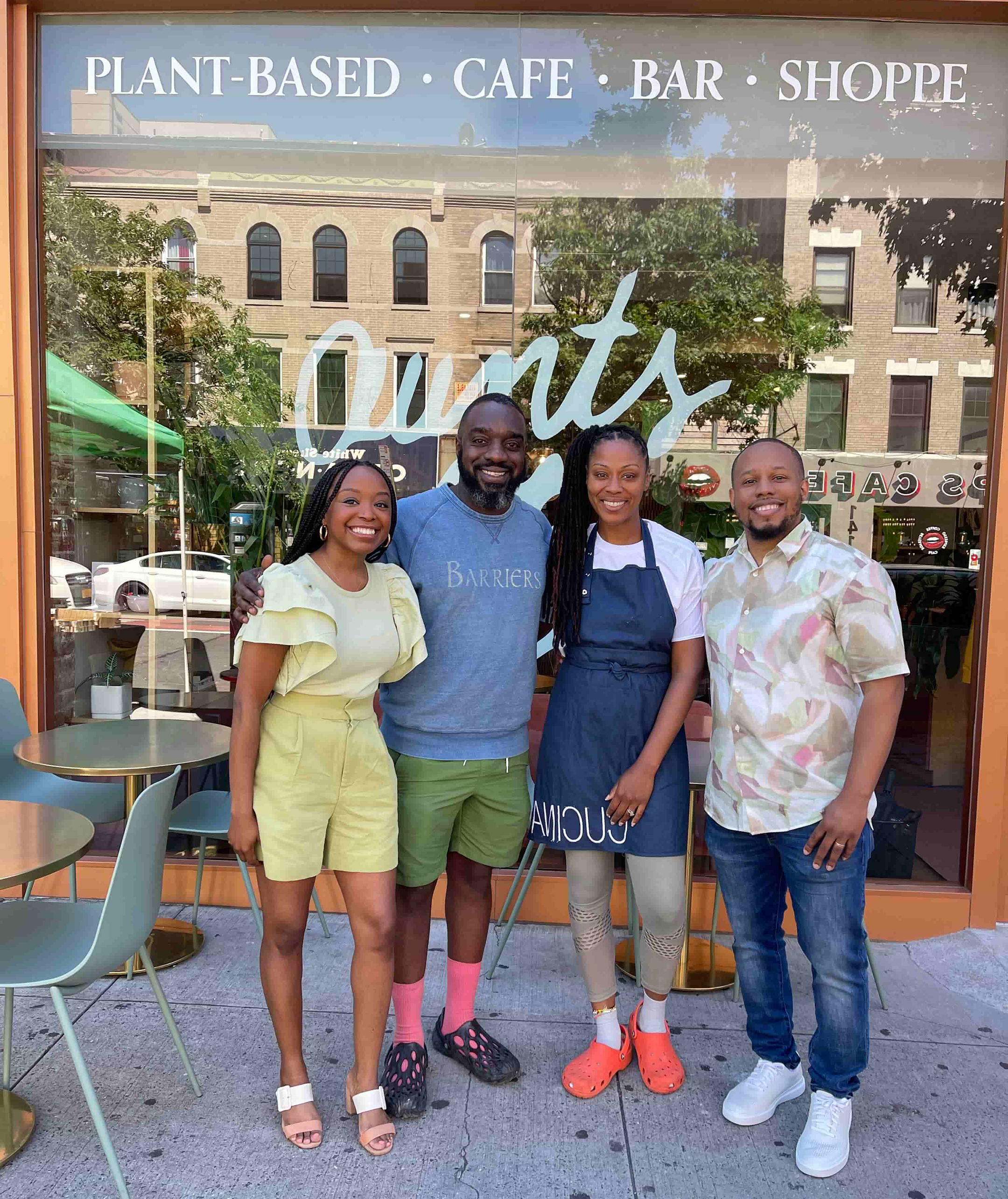 Photo of four people standing in front of a cafe smiling for the camera