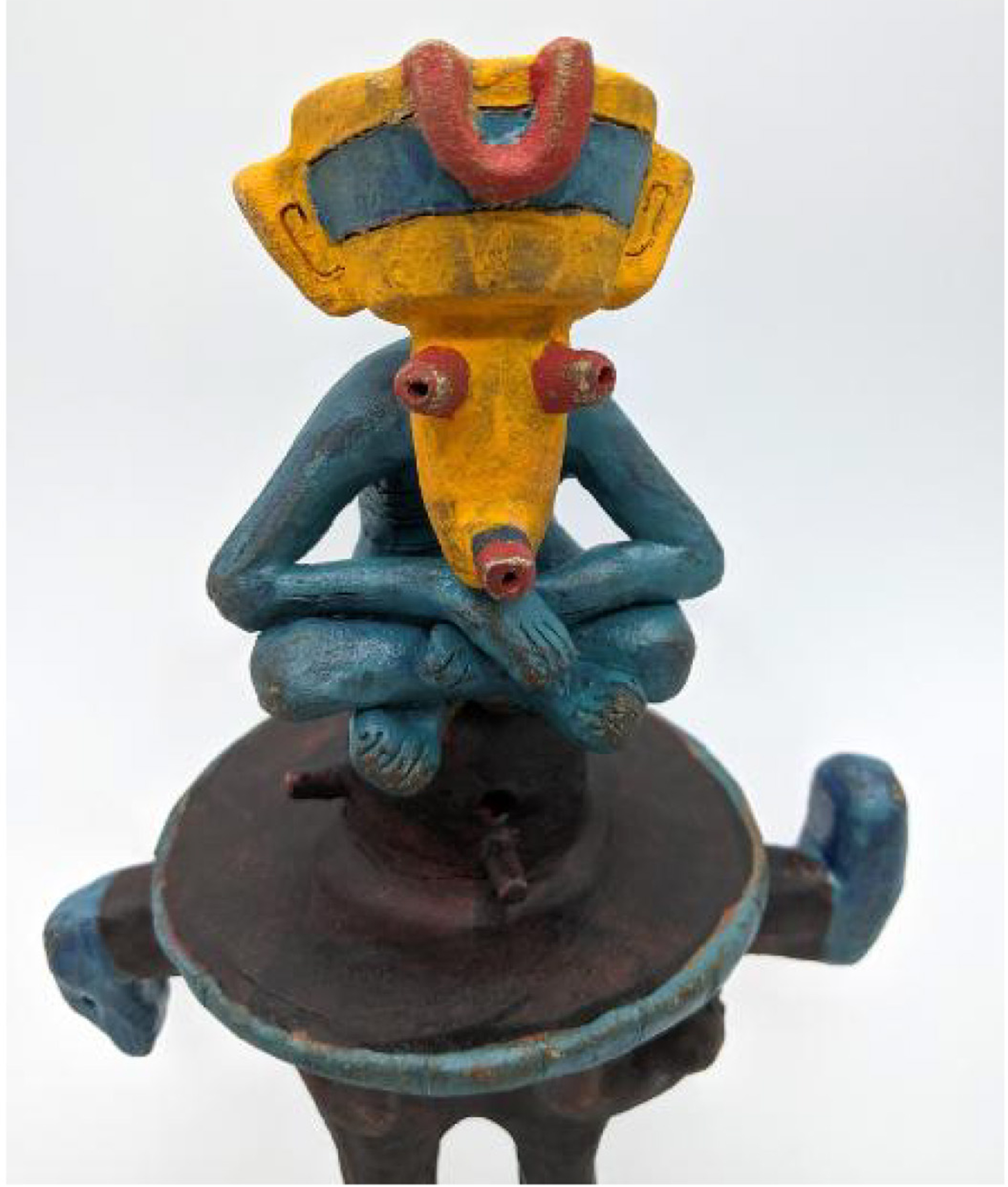 Sculpture of a seated green creature with yellow face and red eyes 