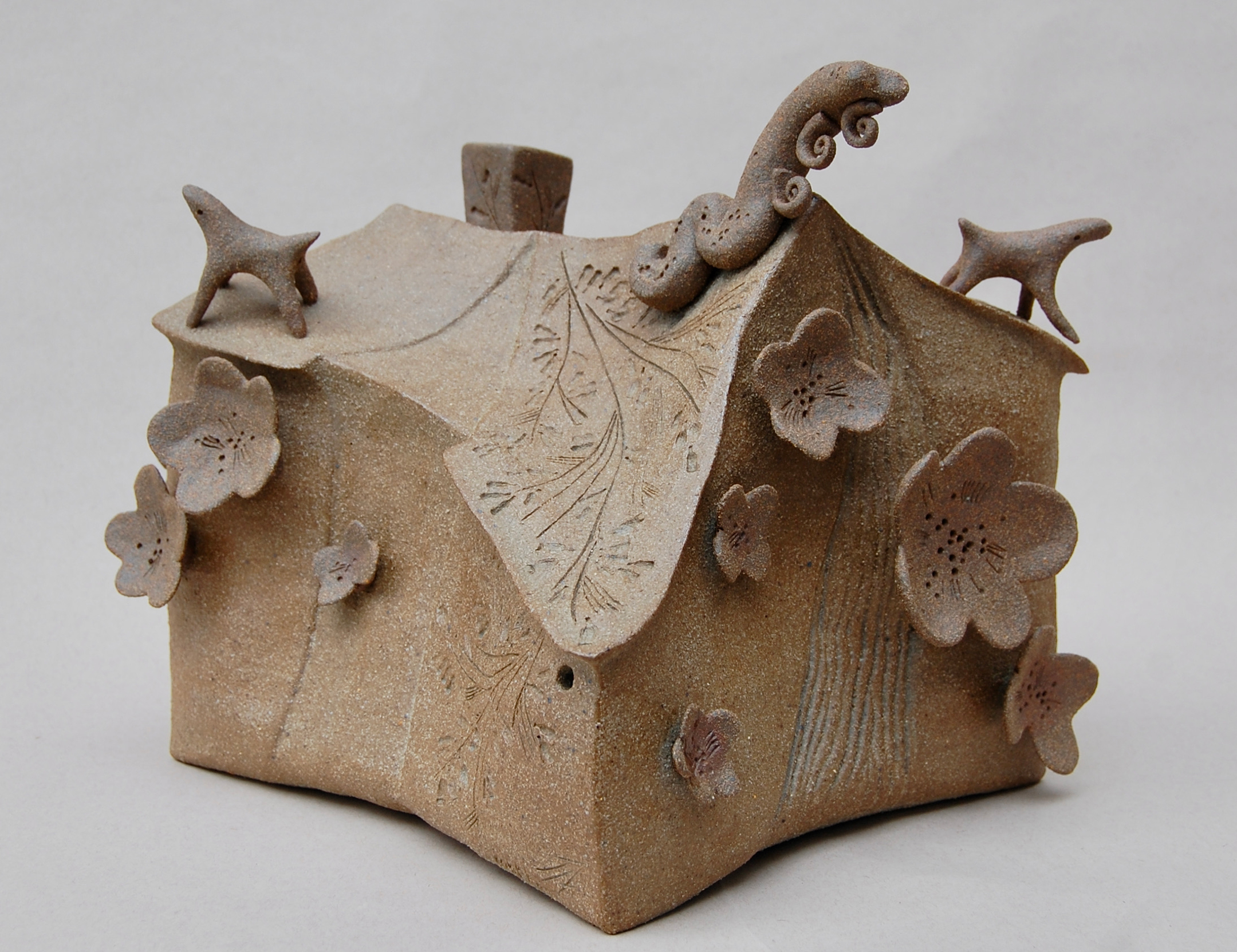 Sculpture of a house with flower and animal shapes attached in a sandy brown
