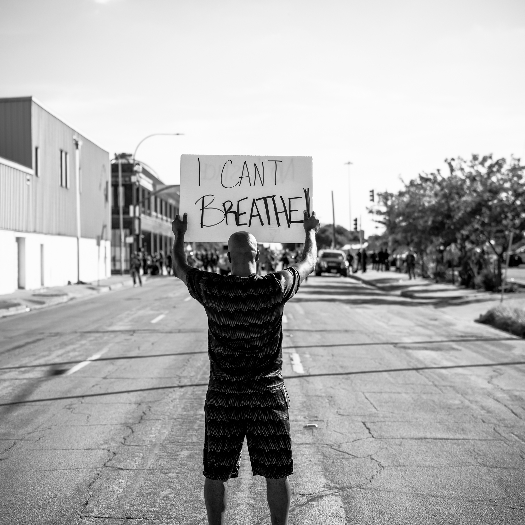 Black and white photo of a black man in a black t-shirt holding a sign that reads I Can't Breathe