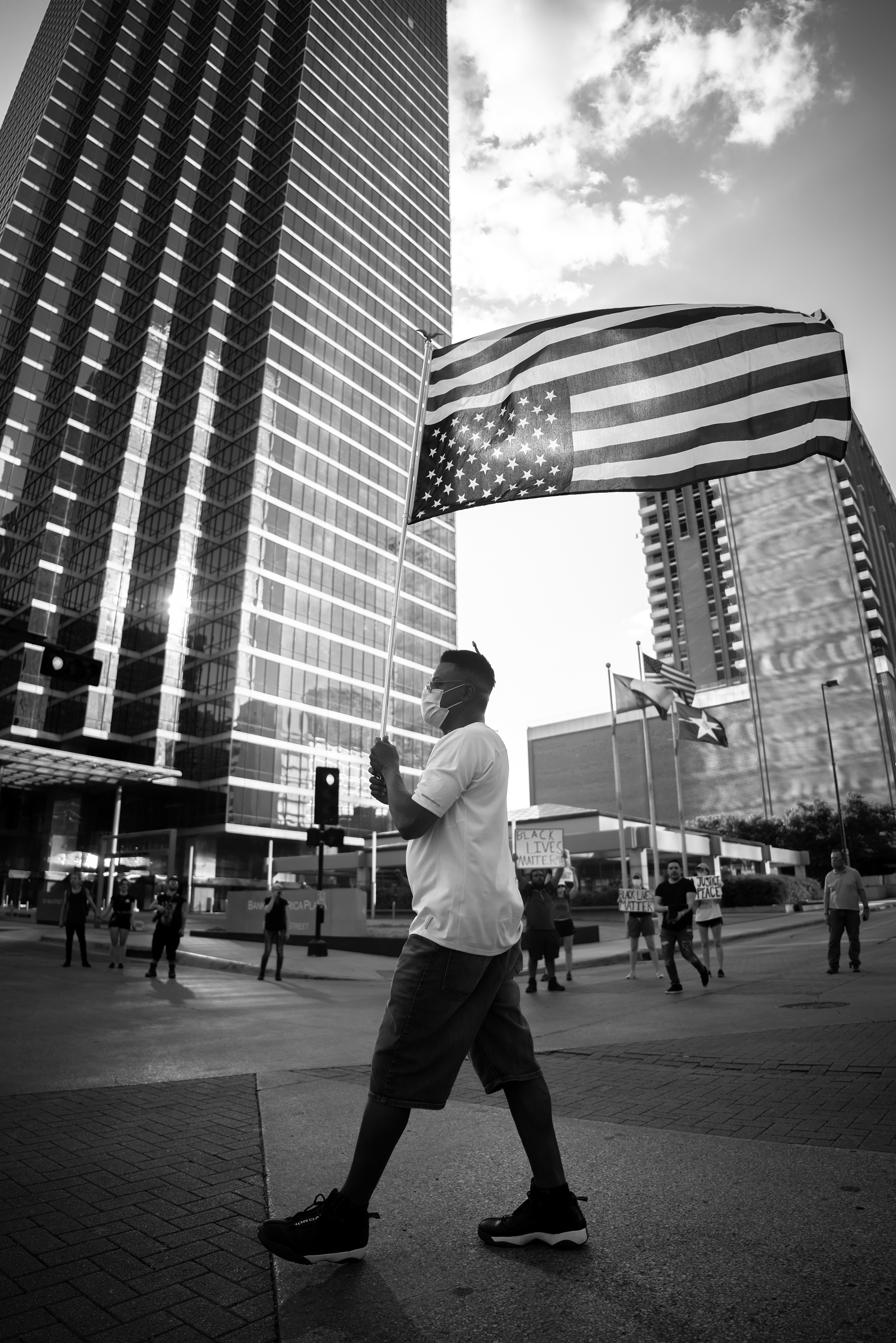 Black and white photo of a black man in a white t-shirt and face mask carrying an upside down American flag