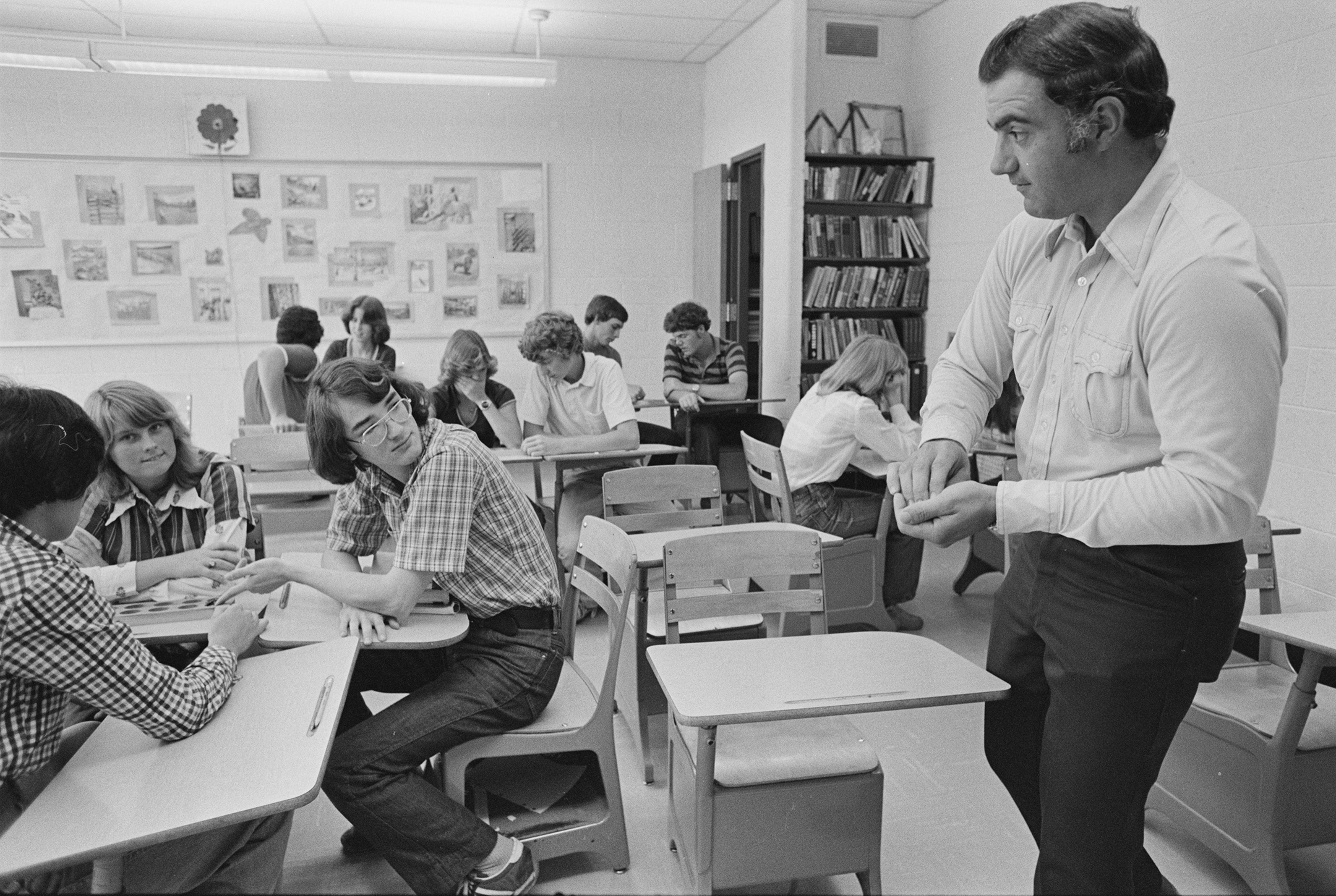 Black and white photograph of a male teacher at the front of a high school classroom teaching students sitting at desks