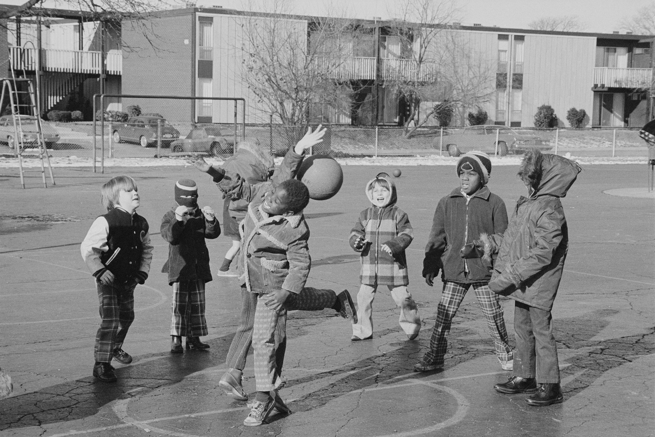 Black and white photograph of elementary school kids playing with a ball outside