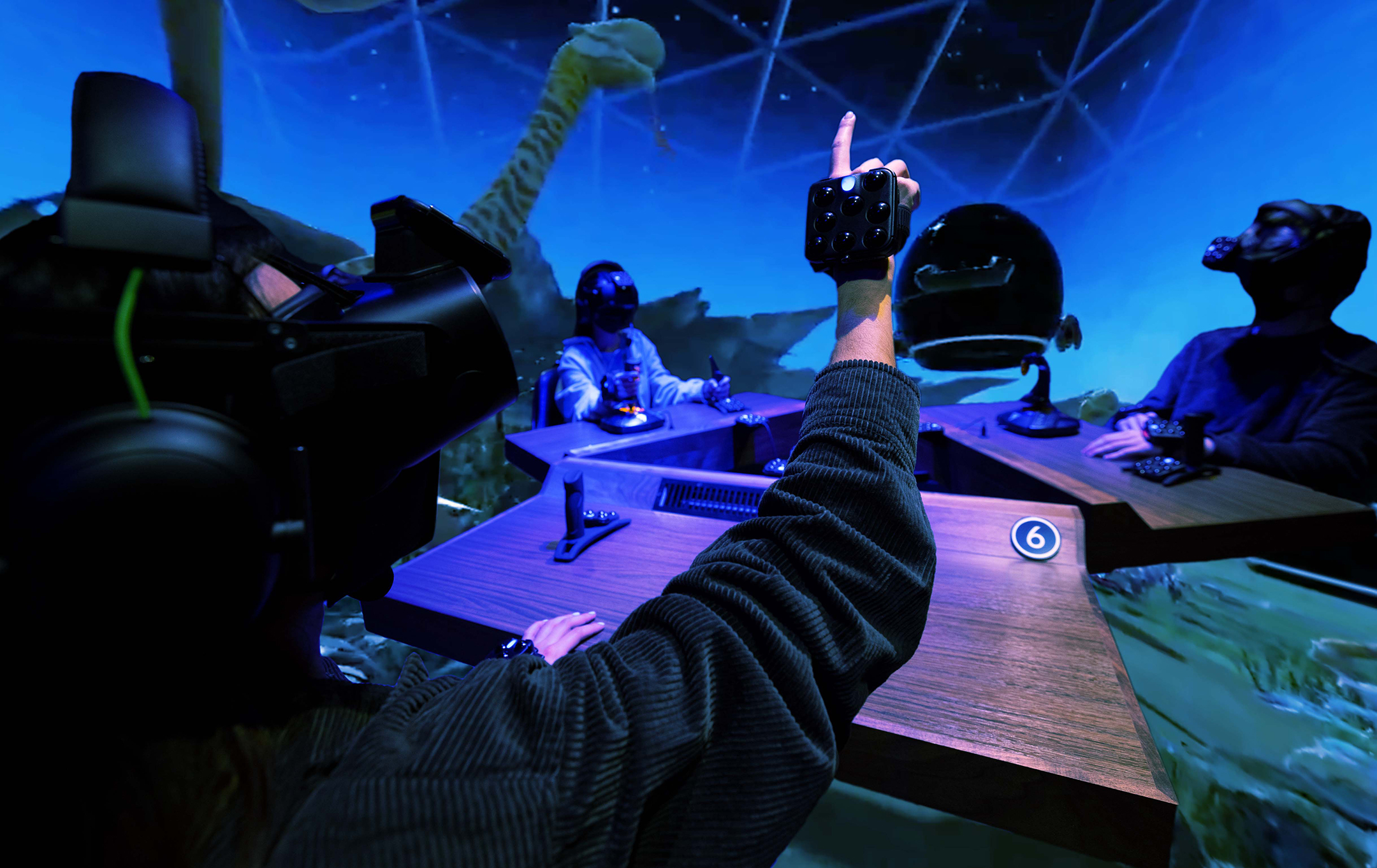 Rendering of three college students, all seated at desks and wearing virtual reality headsets, interacting with a virtual world of dinosaurs and space scenes