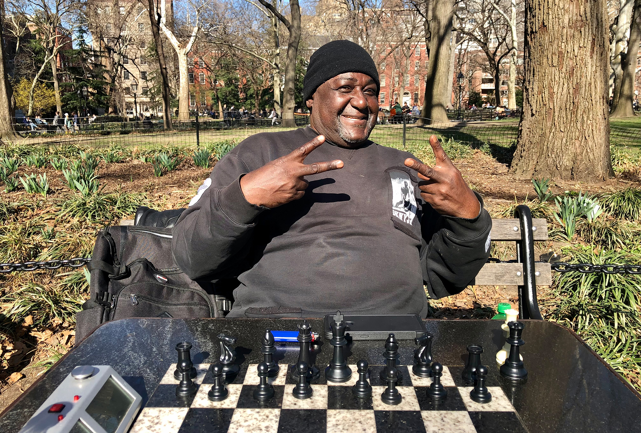 Older black man smiles and poses in front of an outdoor chess board
