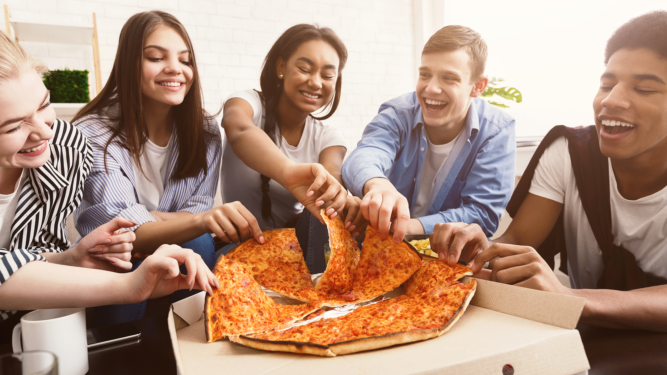 Happy students eating pizza and chatting at home