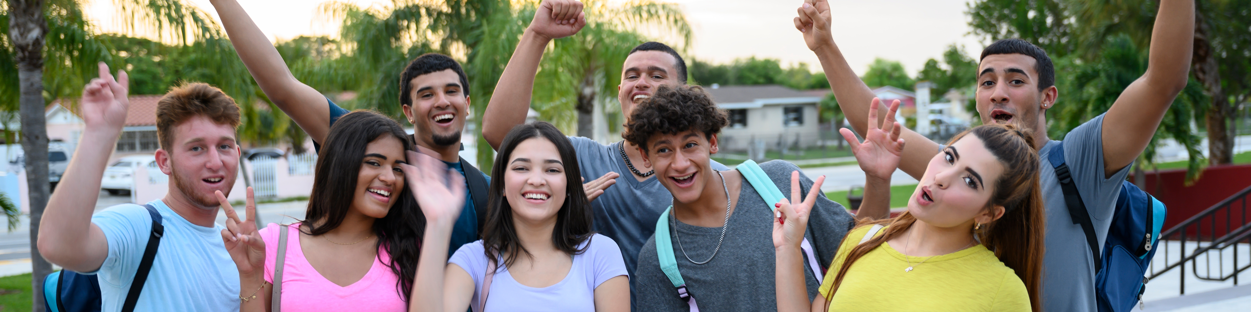 Playful group close-up of Hispanic teenagers laughing and gesturing as they look at camera outside their high school.