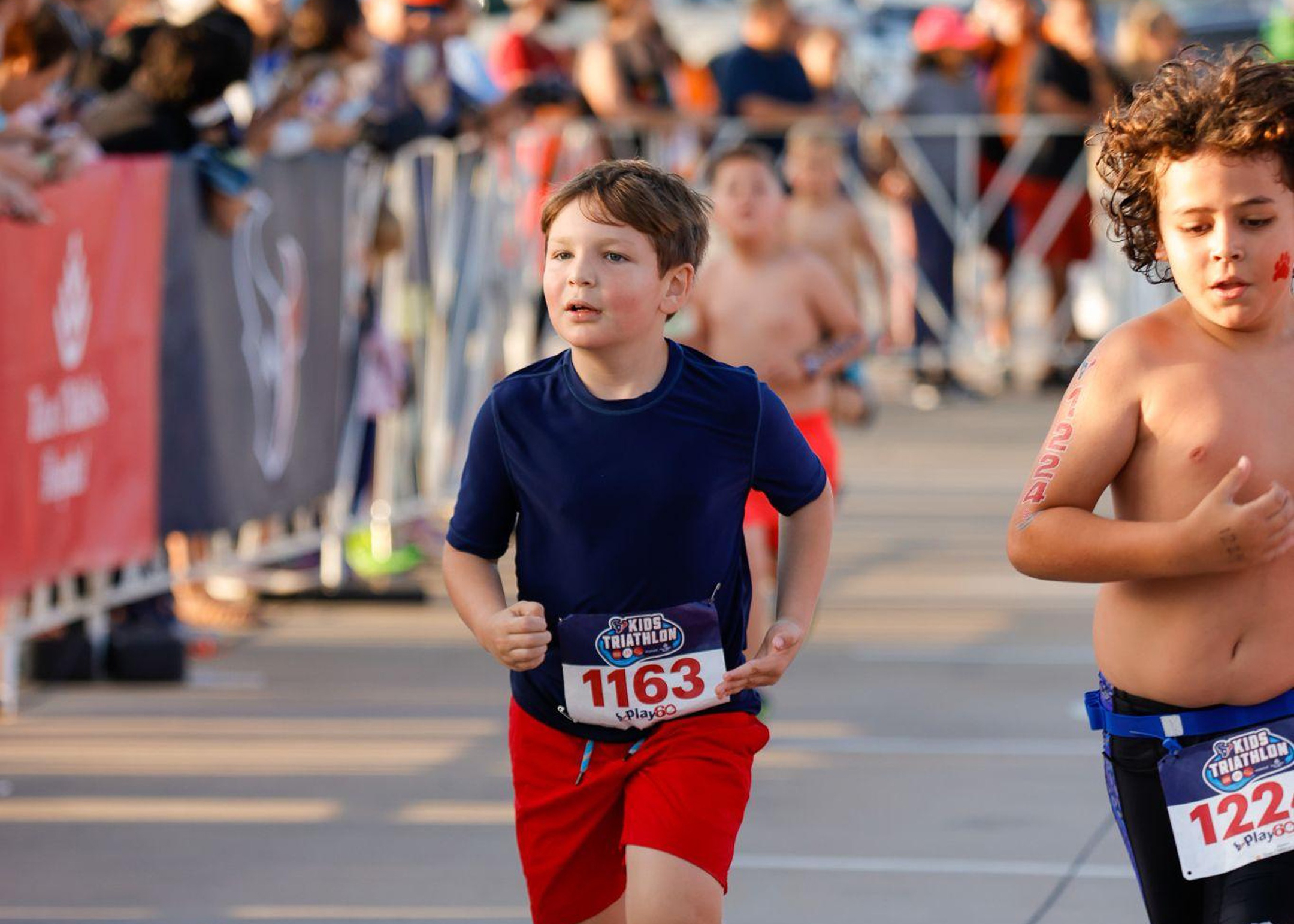 Photo of two boys running a race, one with his shirt on, on the left, and one without a shirt, on the right