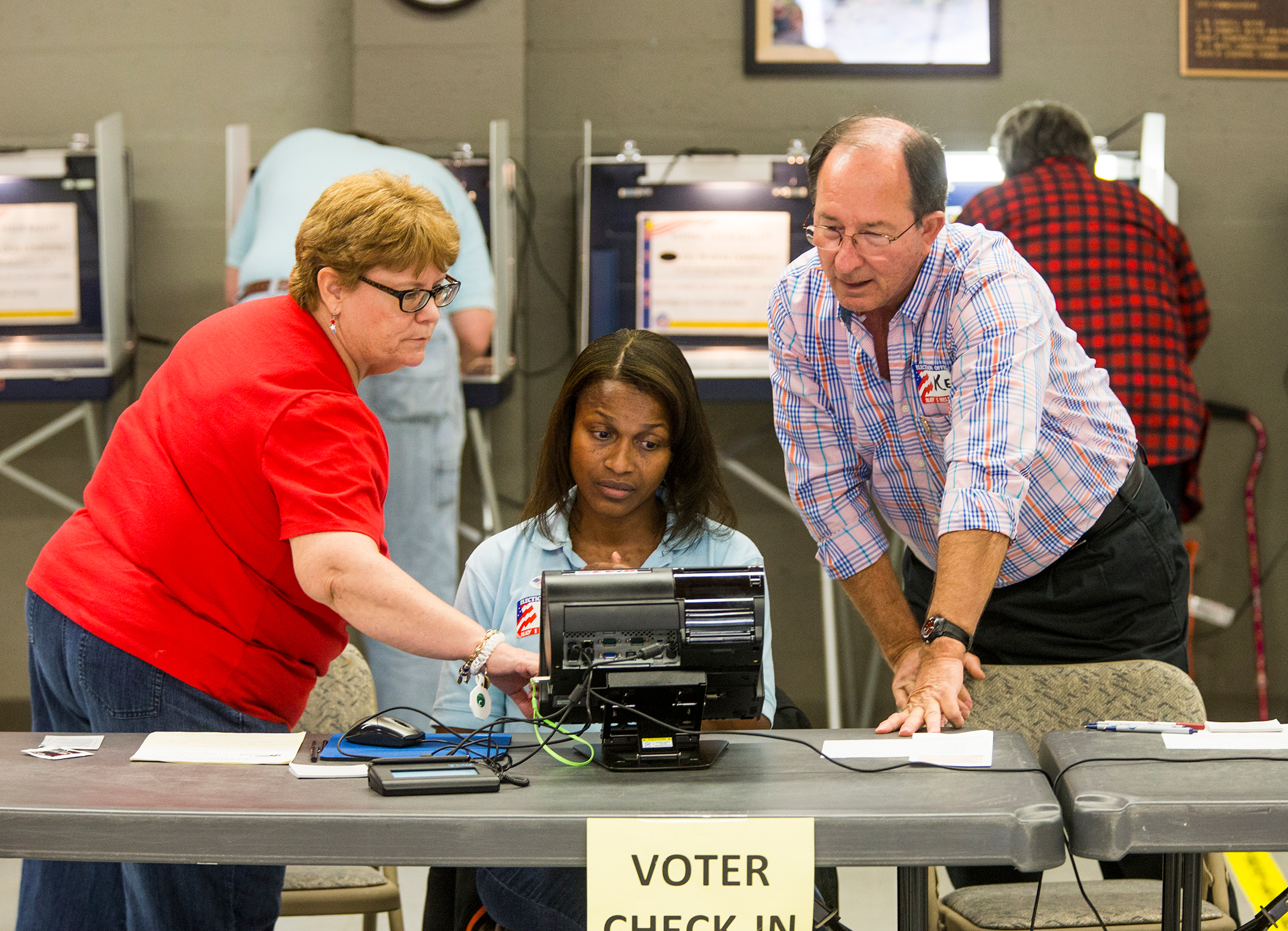 Three people, two women and a man, look at and point at a screen in an election polling place