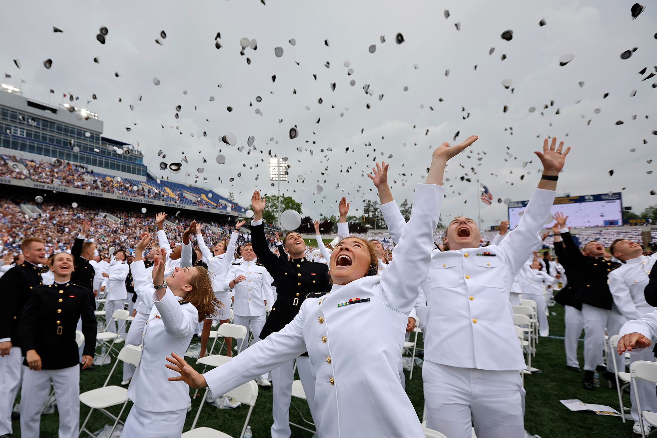 Naval Academy graduates smiling and throwing their caps in the air