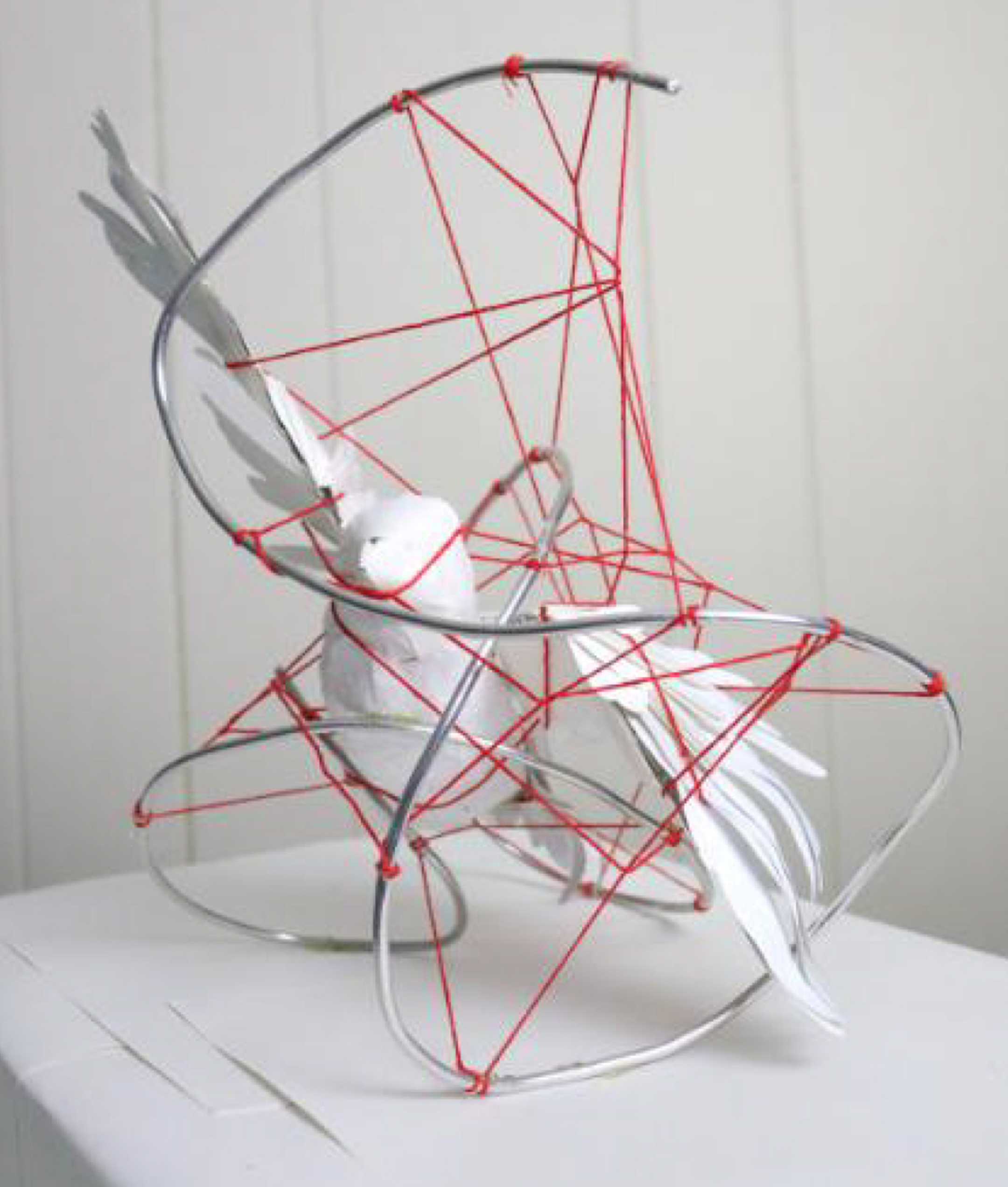 Sculpture of a white bird snared in a tangle of red string