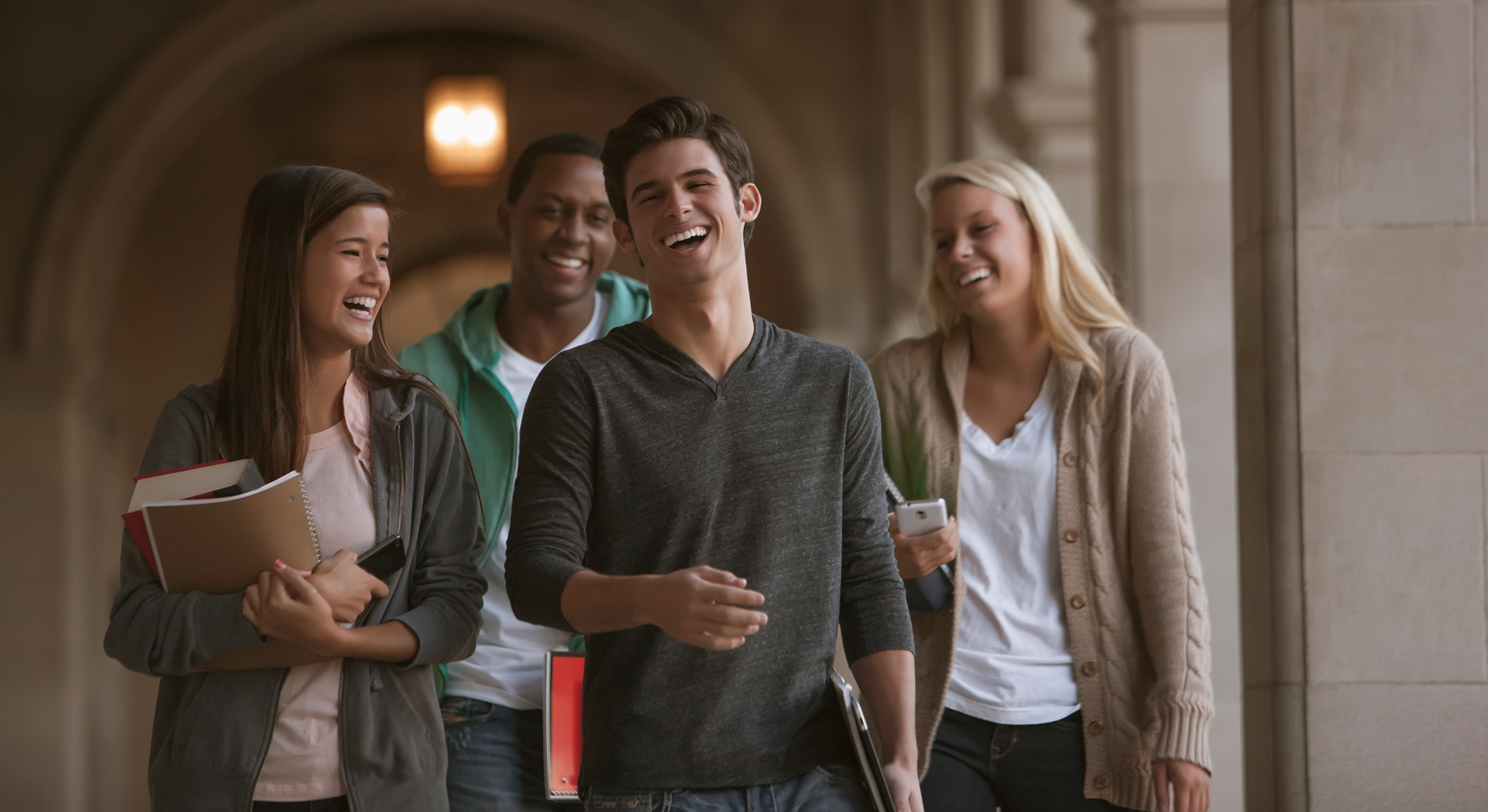 Four college students, 2 male 2 female, smile and laugh as they walk along campus
