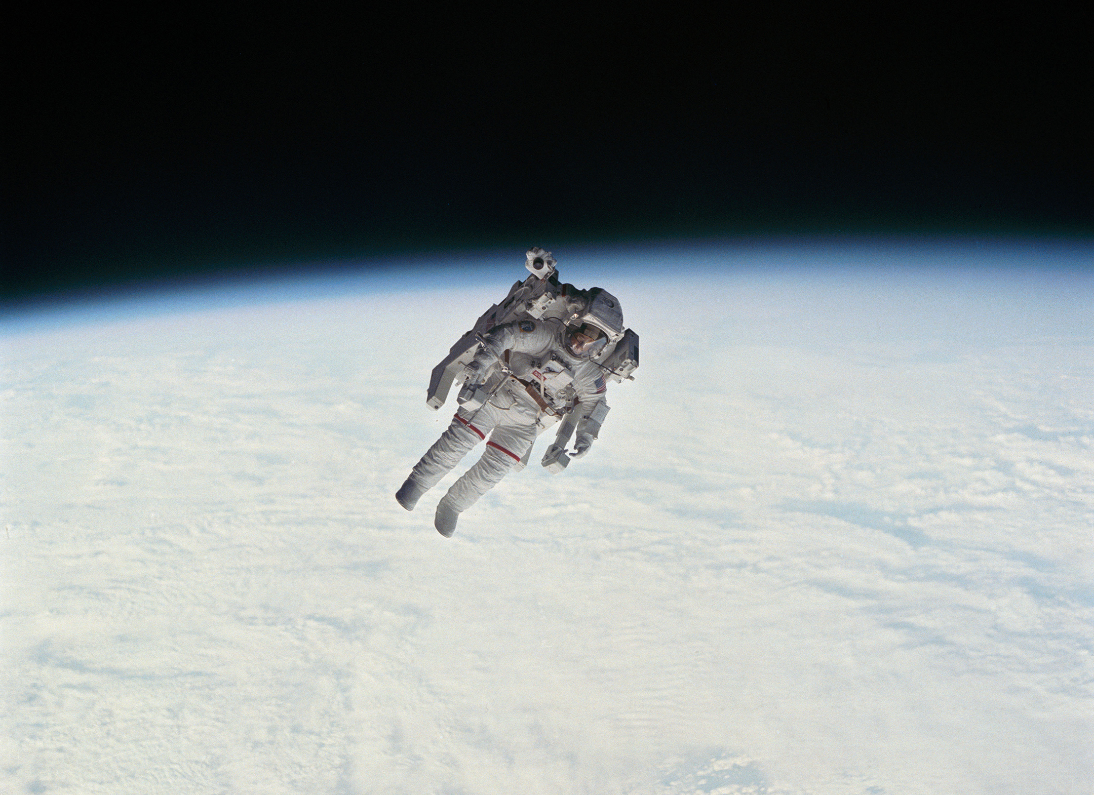Astronaut performing a spacewalk above a cloud-covered earth