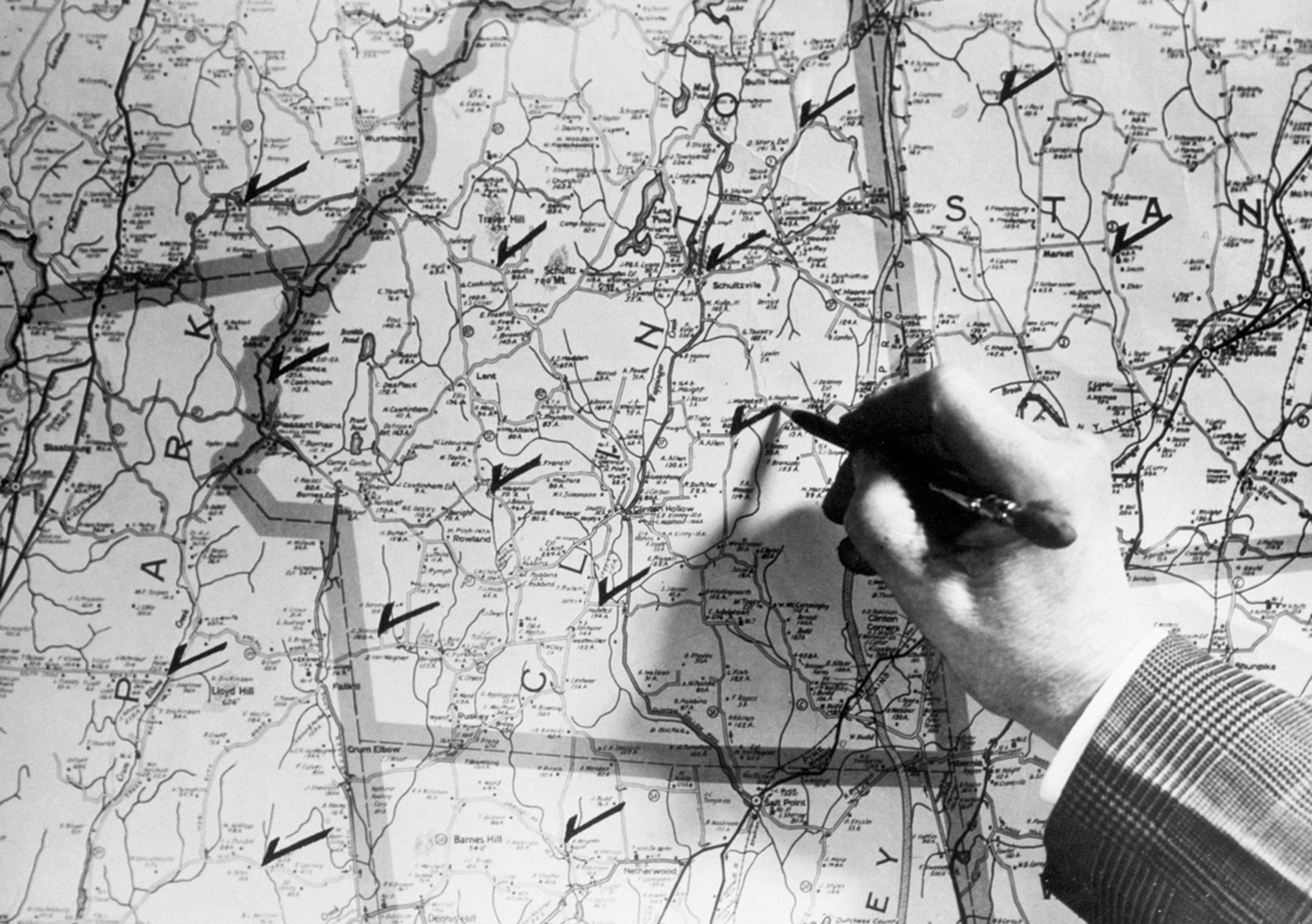 Black and white photo of a man's hand checking off towns on map in 1940s