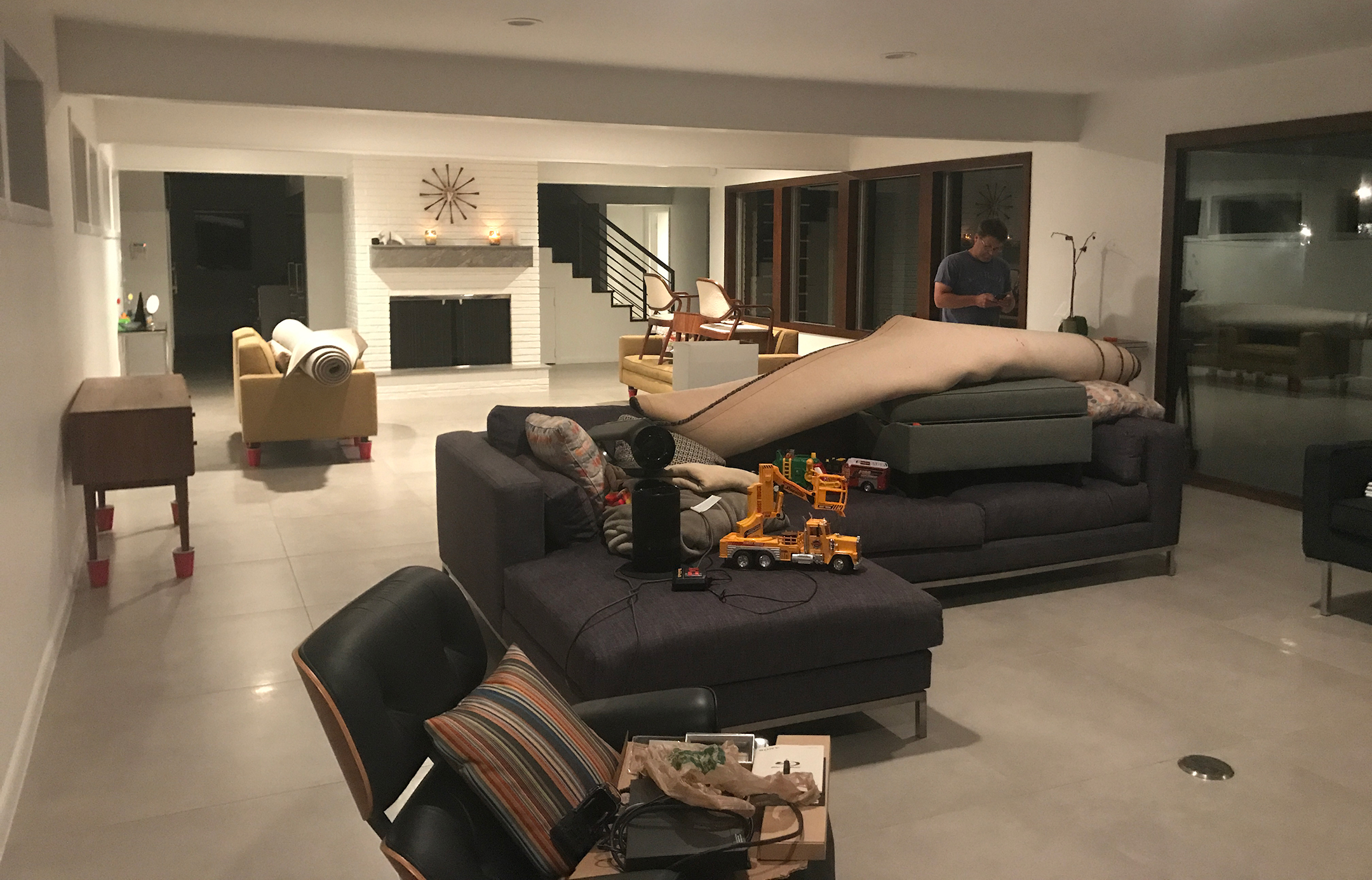 Photo of a living room with couches and chairs covered in elevated toys, furniture, and rugs