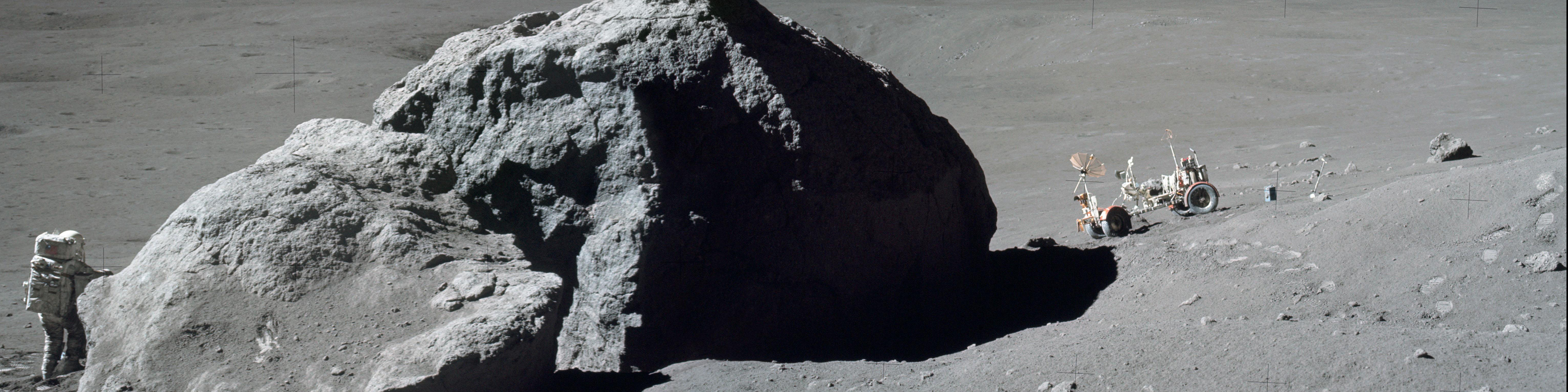 Astronaut walking on the moon, holds onto a massive boulder, while his rover waits on the other side of the rock